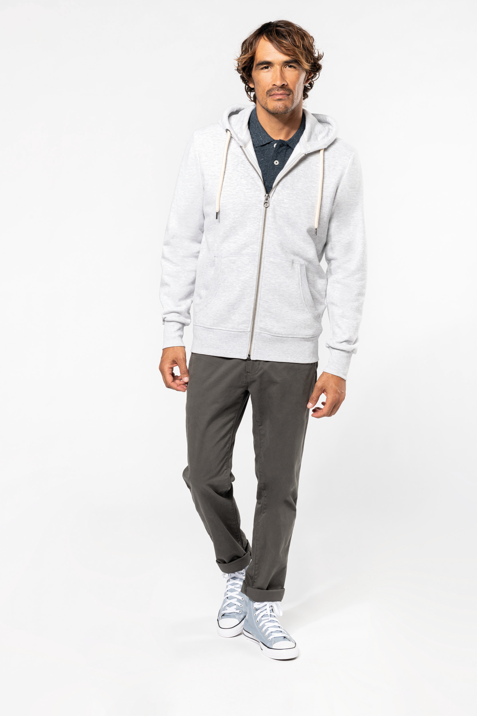 Hombre de pie en estudio vistiendo sudadera gris con capucha, polo oscuro, pantalones chinos y zapatillas altas.