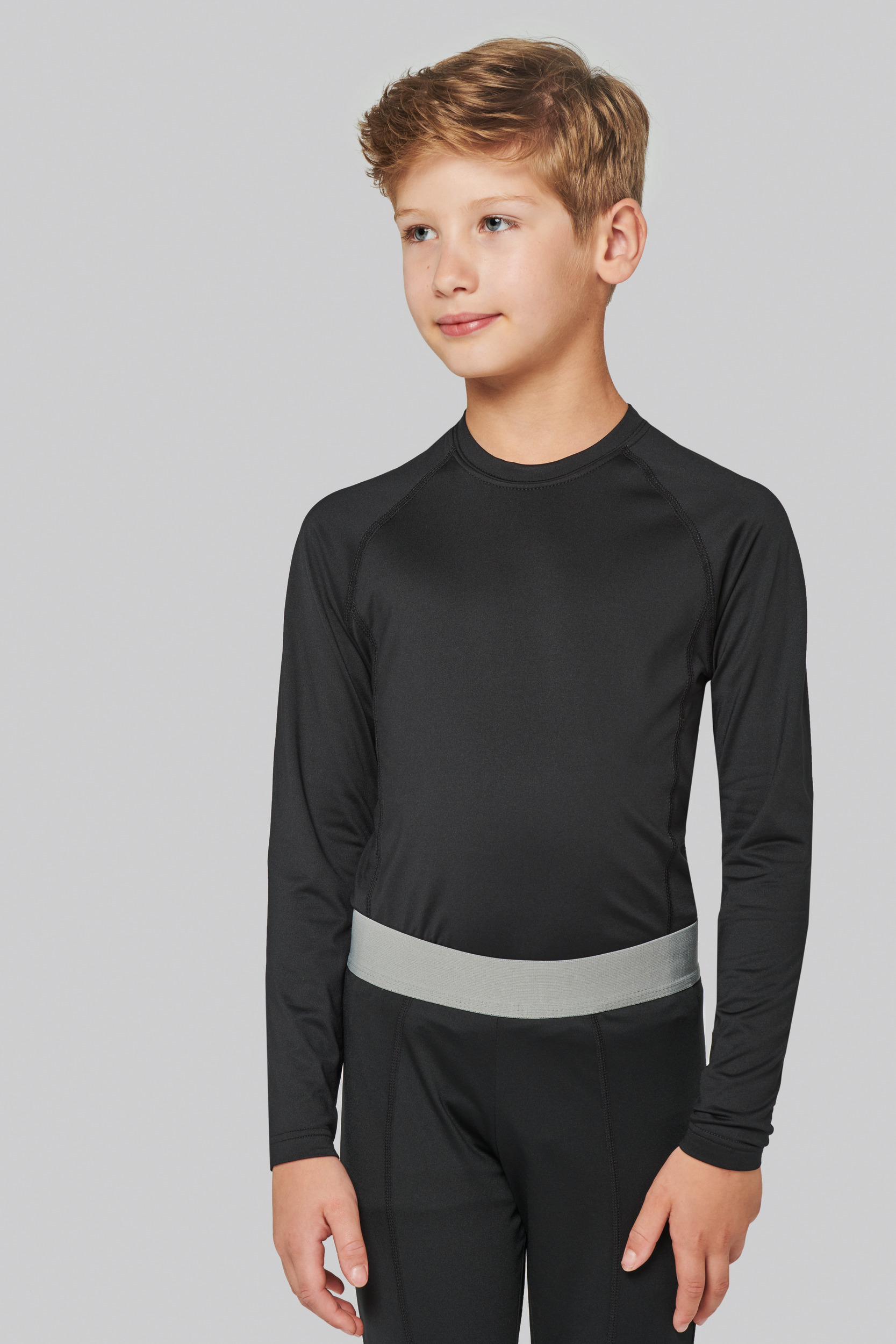 niño con camiseta y pantalones negros de deporte de manga larga mirando hacia la derecha sobre fondo neutro