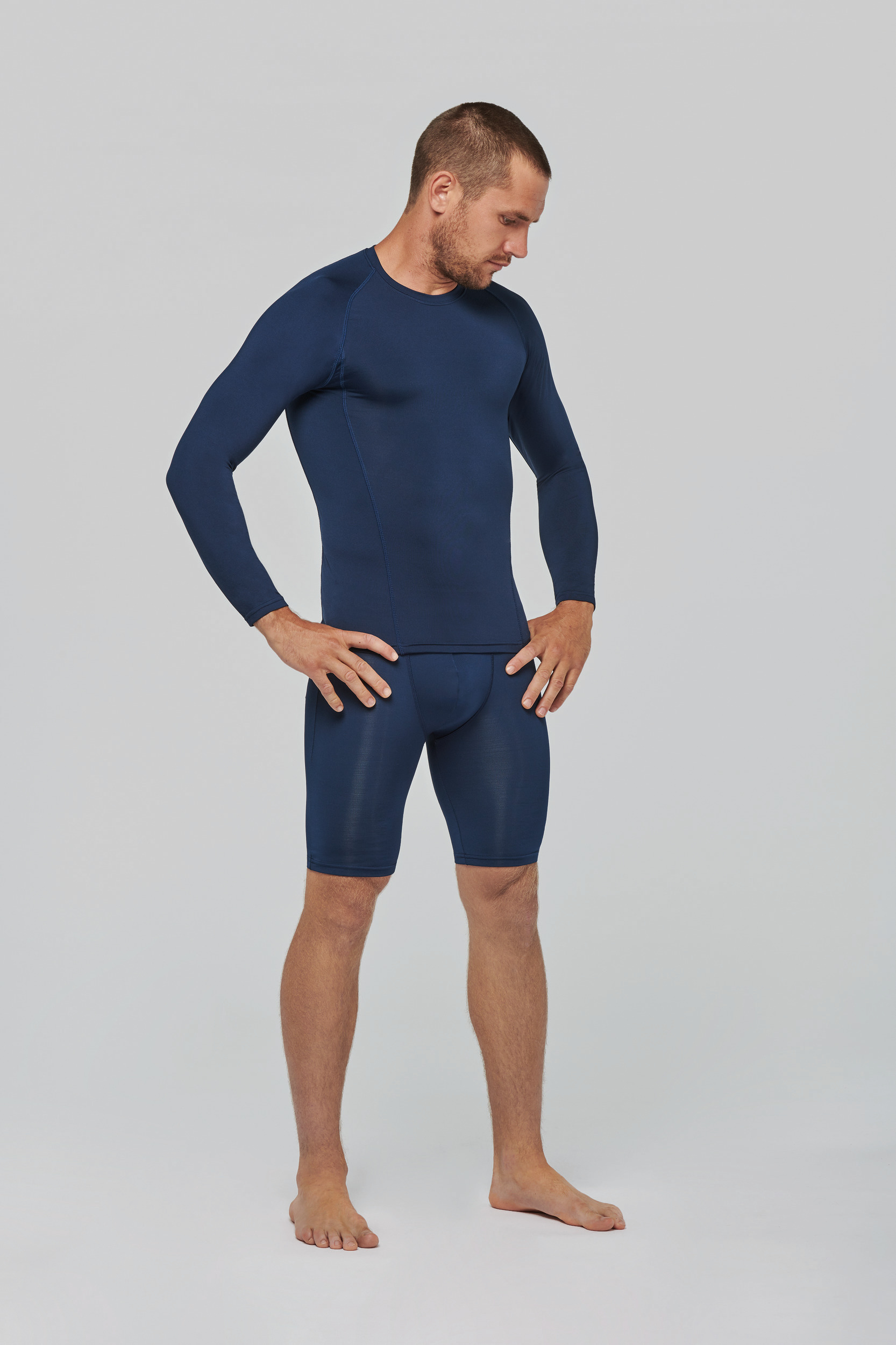 hombre en pose de modelo con camiseta y mallas térmicas ajustadas azules sobre fondo blanco
