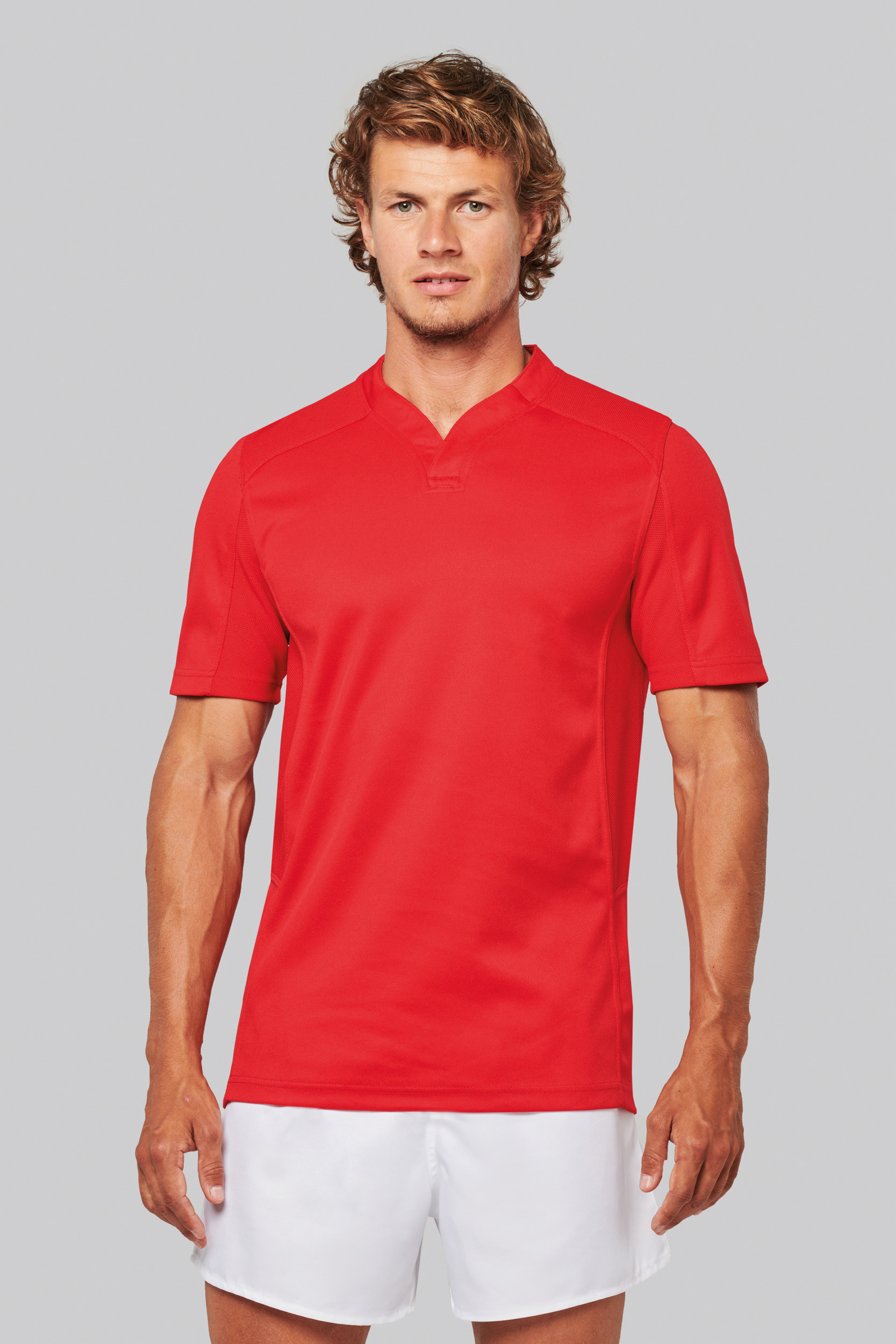 Hombre con camiseta deportiva roja y pantalones cortos blancos sobre fondo gris claro.