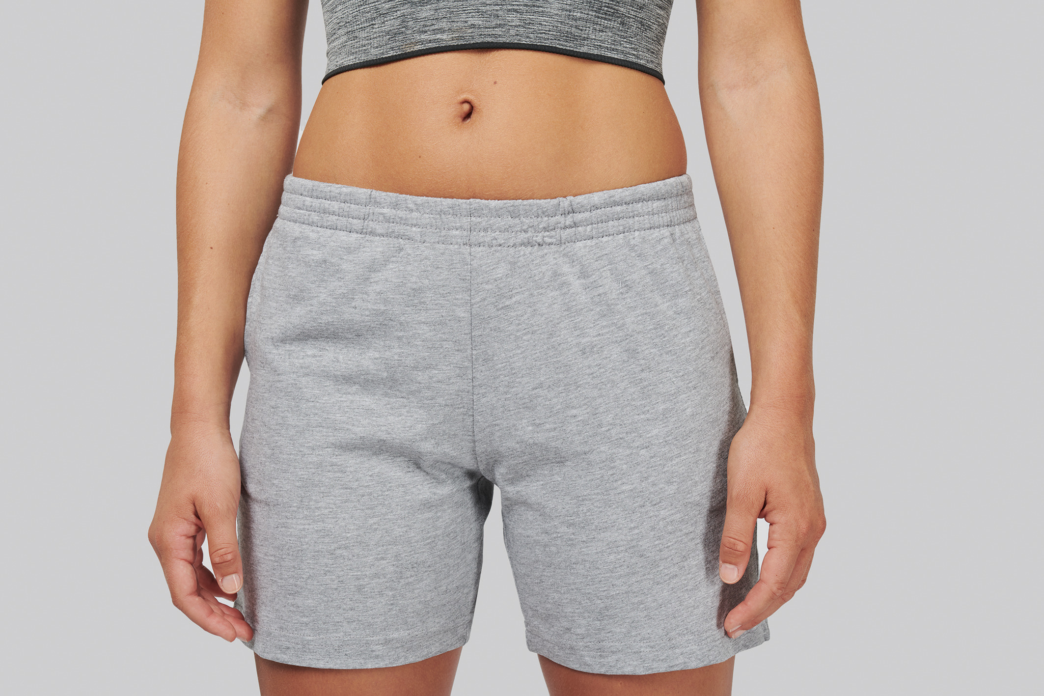 Torso de mujer con top deportivo gris y pantalones cortos grises de tela cómoda