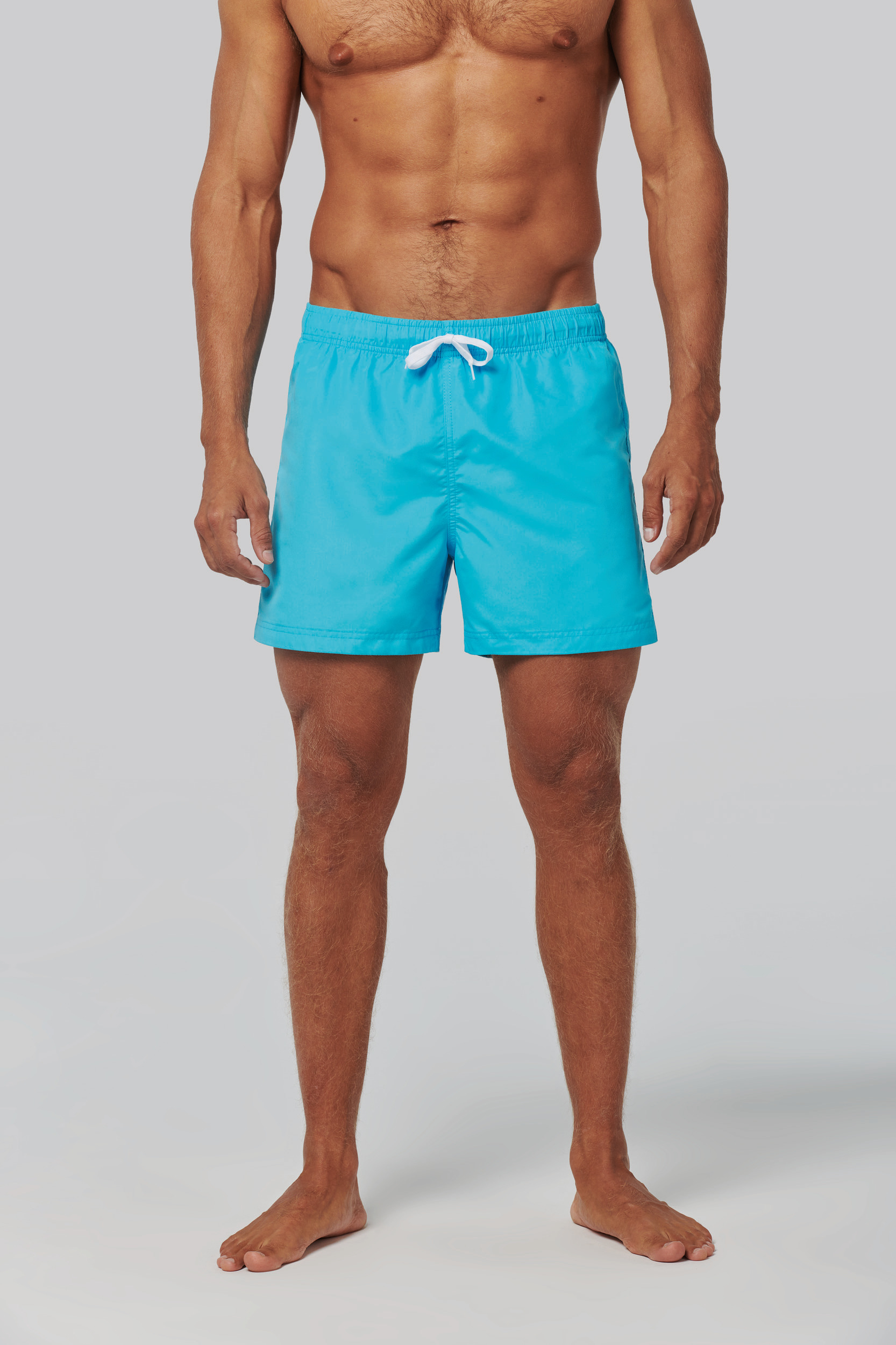 Modelo masculino de pie con bañador azul y cordón blanco sobre fondo gris