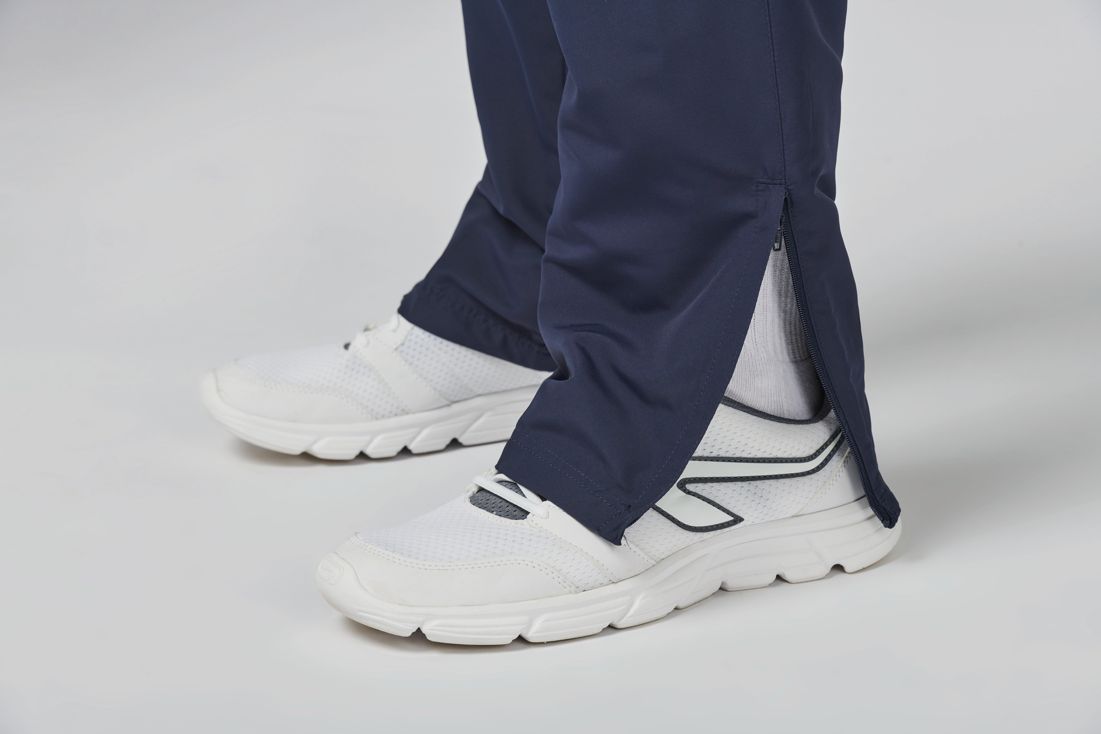 Piernas con pantalón deportivo azul marino con cremallera en el tobillo y zapatillas blancas.