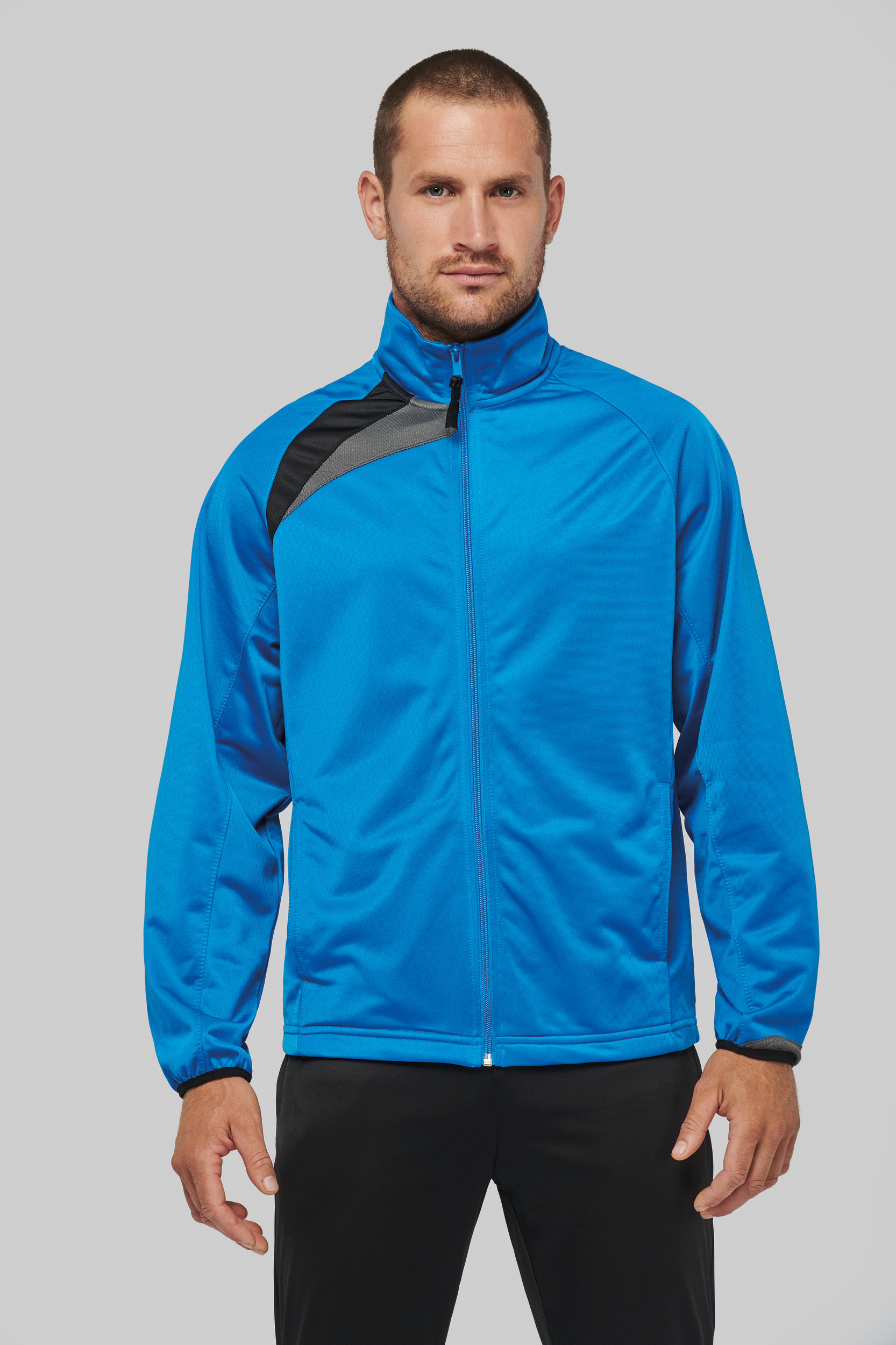 Hombre con chaqueta deportiva azul de cremallera sobre fondo gris.