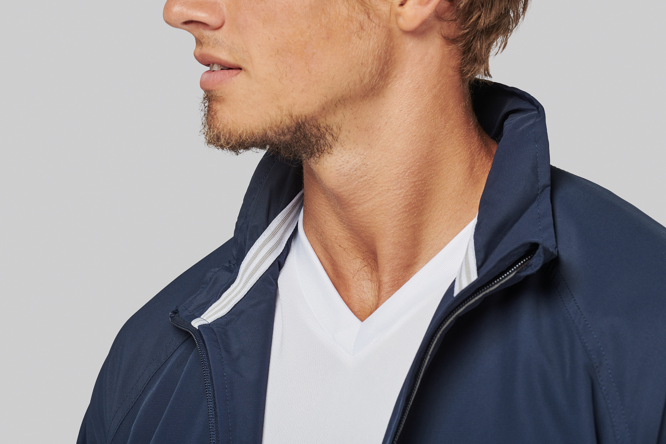 Perfil de un hombre con barba incipiente vistiendo una camiseta blanca de cuello en V y una chaqueta azul marino.