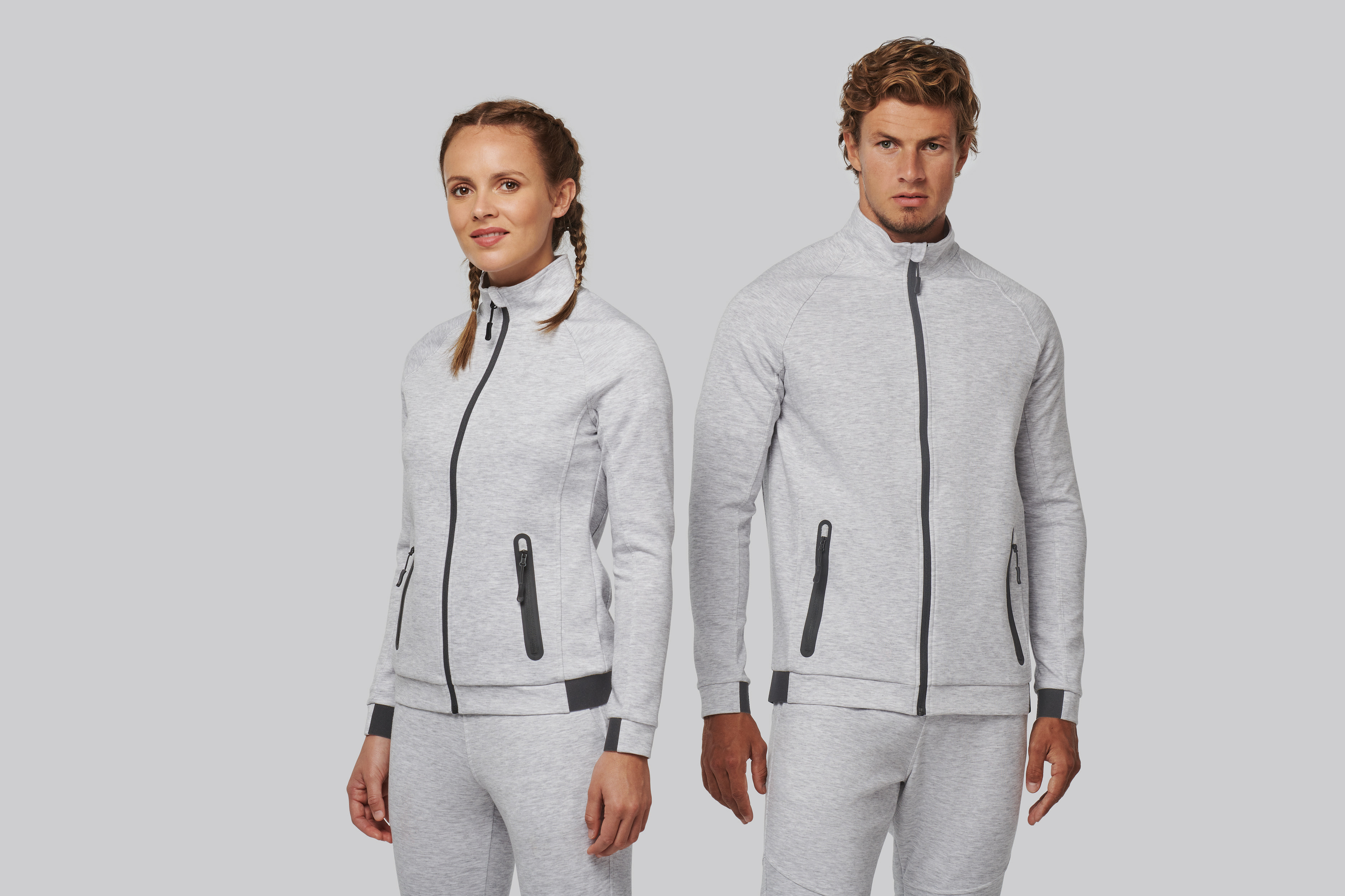 Pareja posando con chándal gris claro de chaqueta y pantalón deportivos con cremallera vertical.