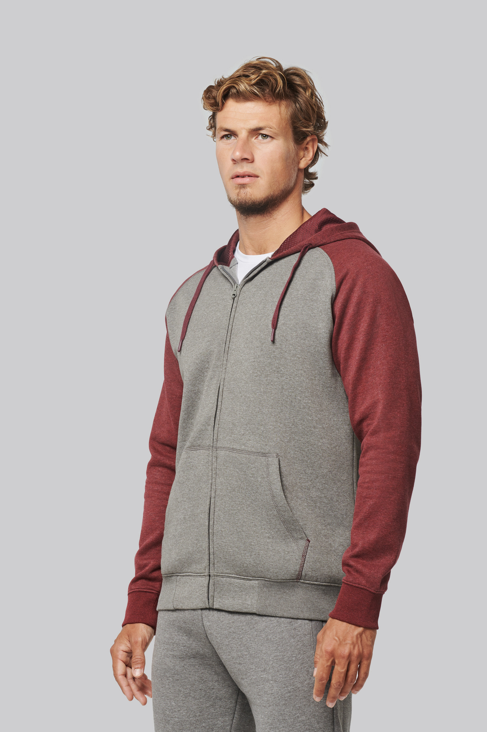 Hombre joven con sudadera con capucha gris y mangas granate sobre fondo neutro