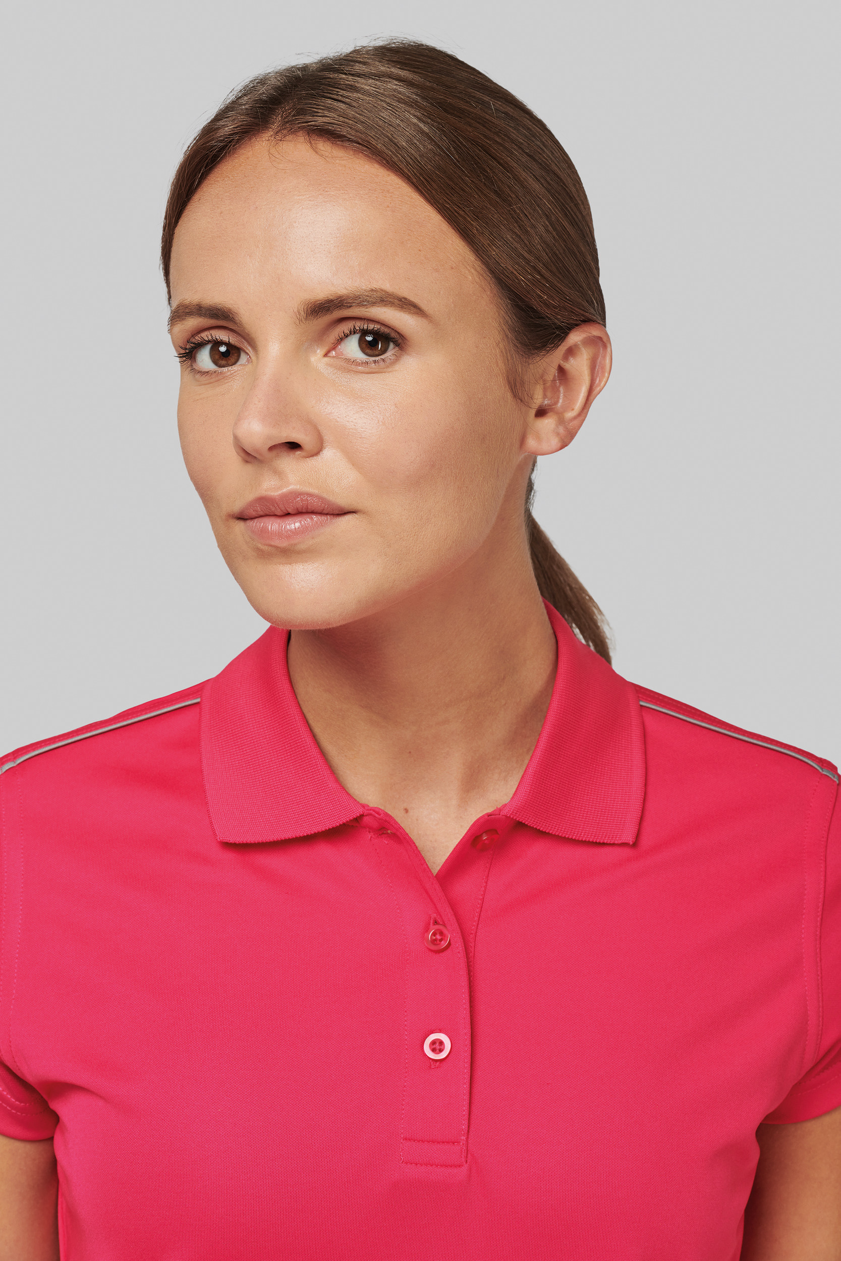 Mujer de rostro sereno con el pelo recogido luciendo un polo rojo sobre fondo neutro.