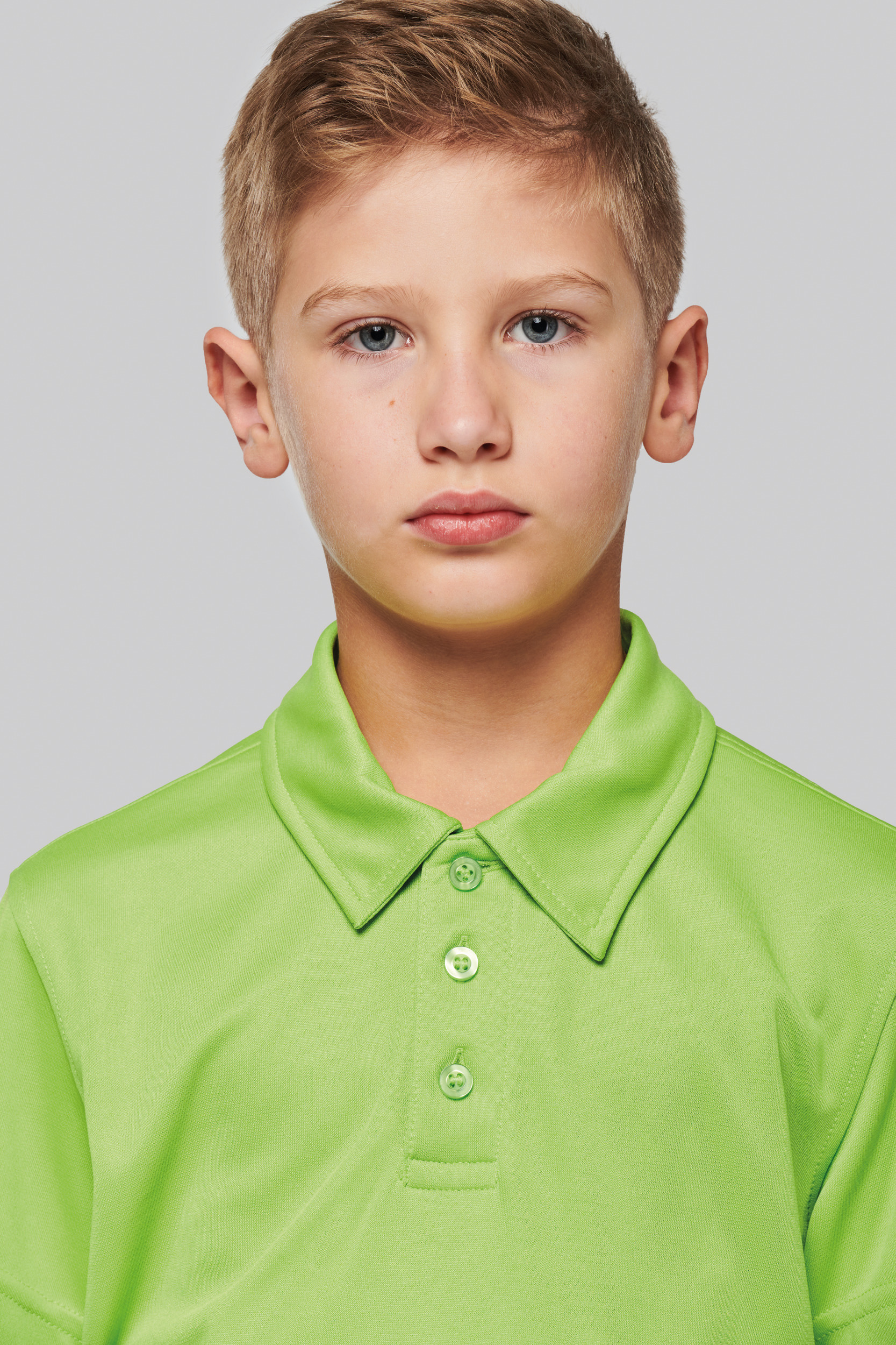 retrato de un niño con camiseta polo verde sobre fondo gris