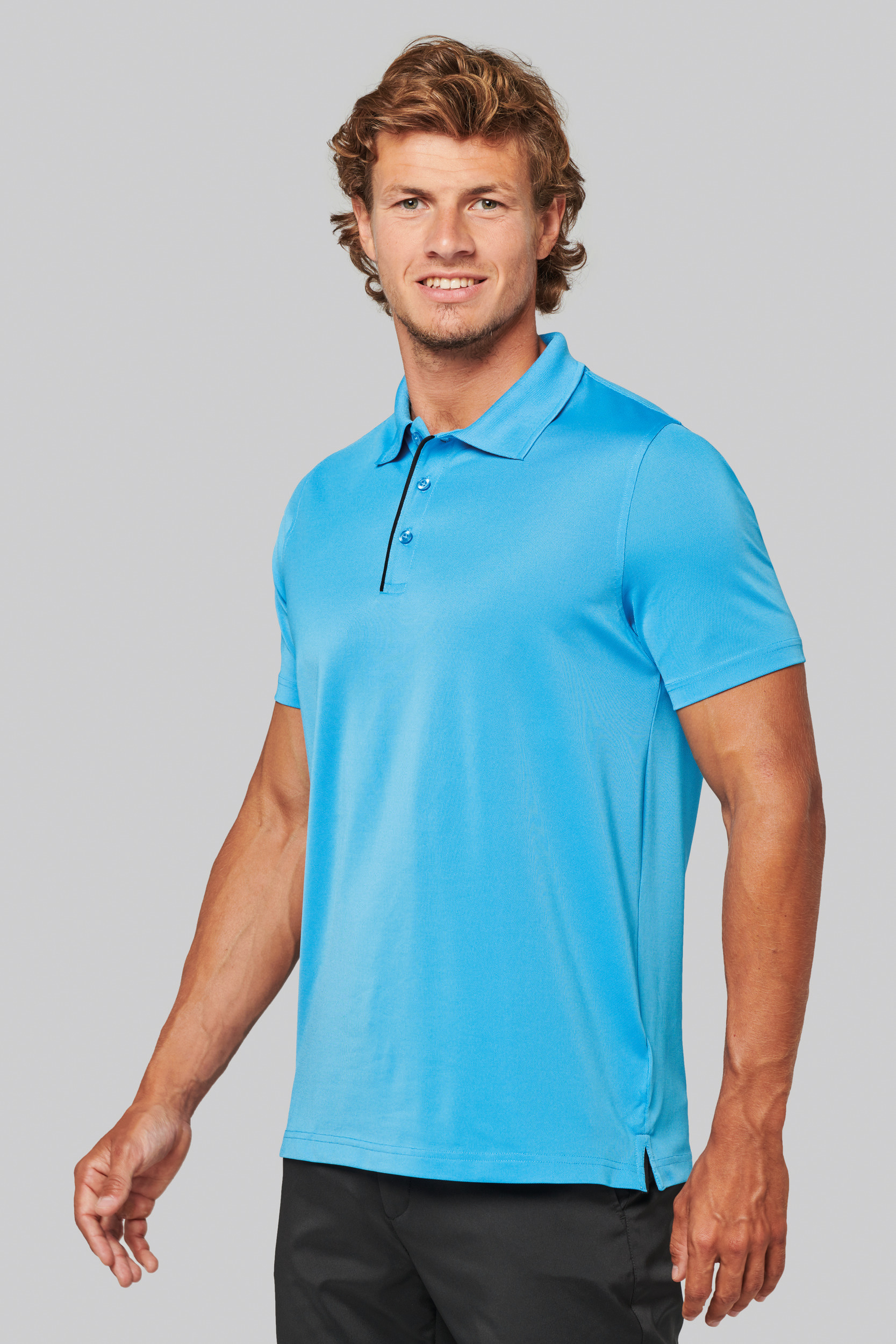 Hombre sonriendo con polo azul y pantalón negro sobre fondo neutro