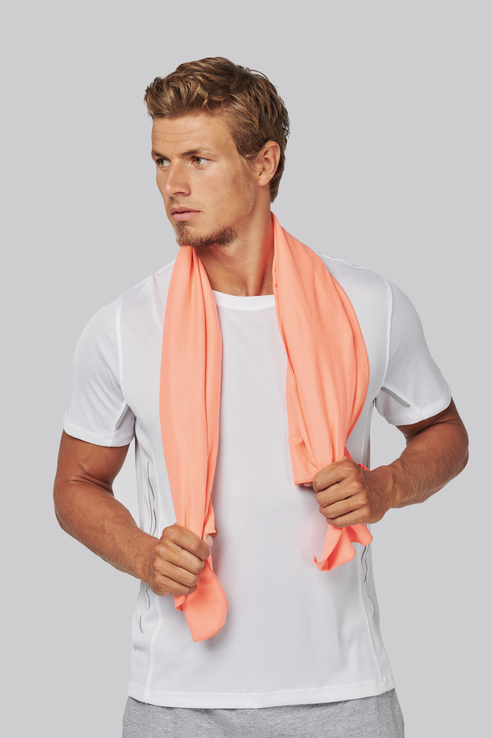 Hombre con camiseta deportiva blanca y toalla de microfibra coral sobre los hombros, mirando hacia la izquierda.