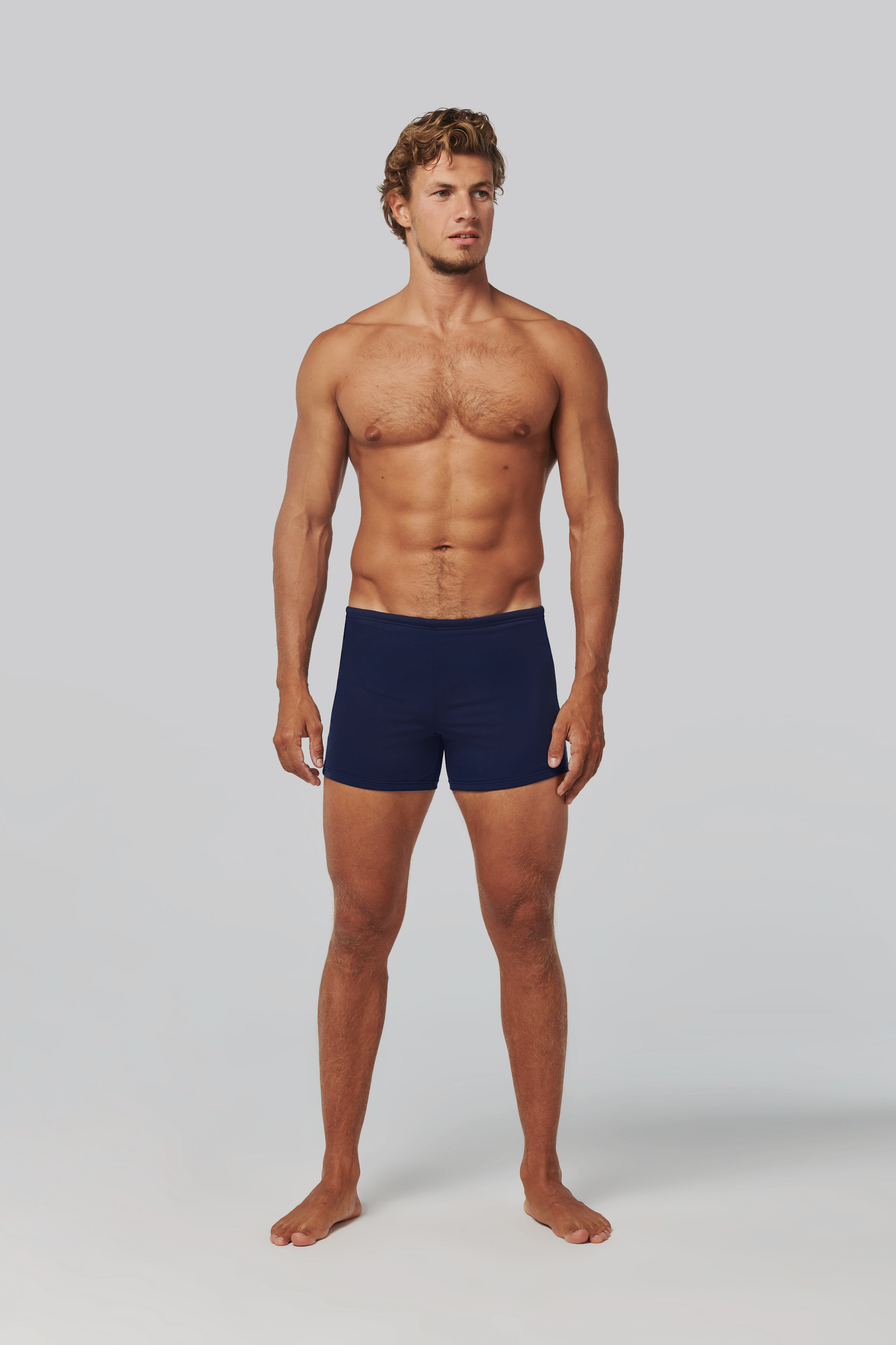 Hombre con físico atlético vistiendo bóxer azul marino sobre fondo gris claro.