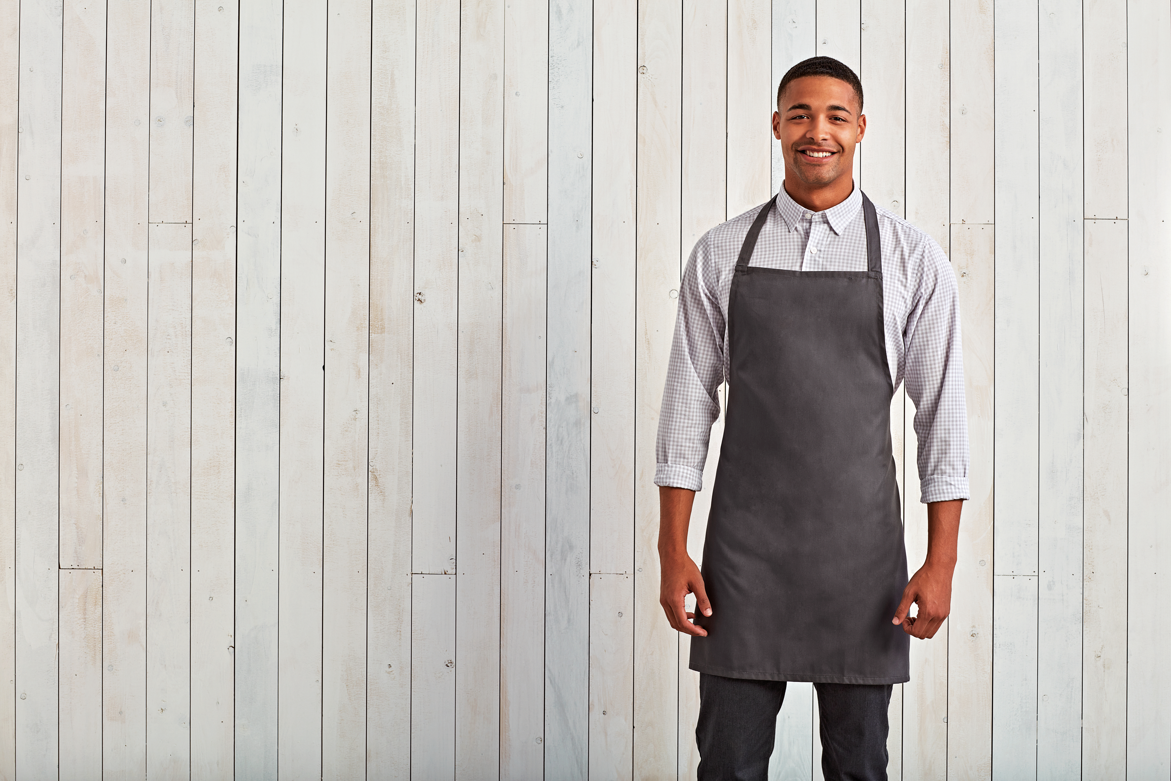 Hombre sonriente con delantal gris junto a pared de madera clara