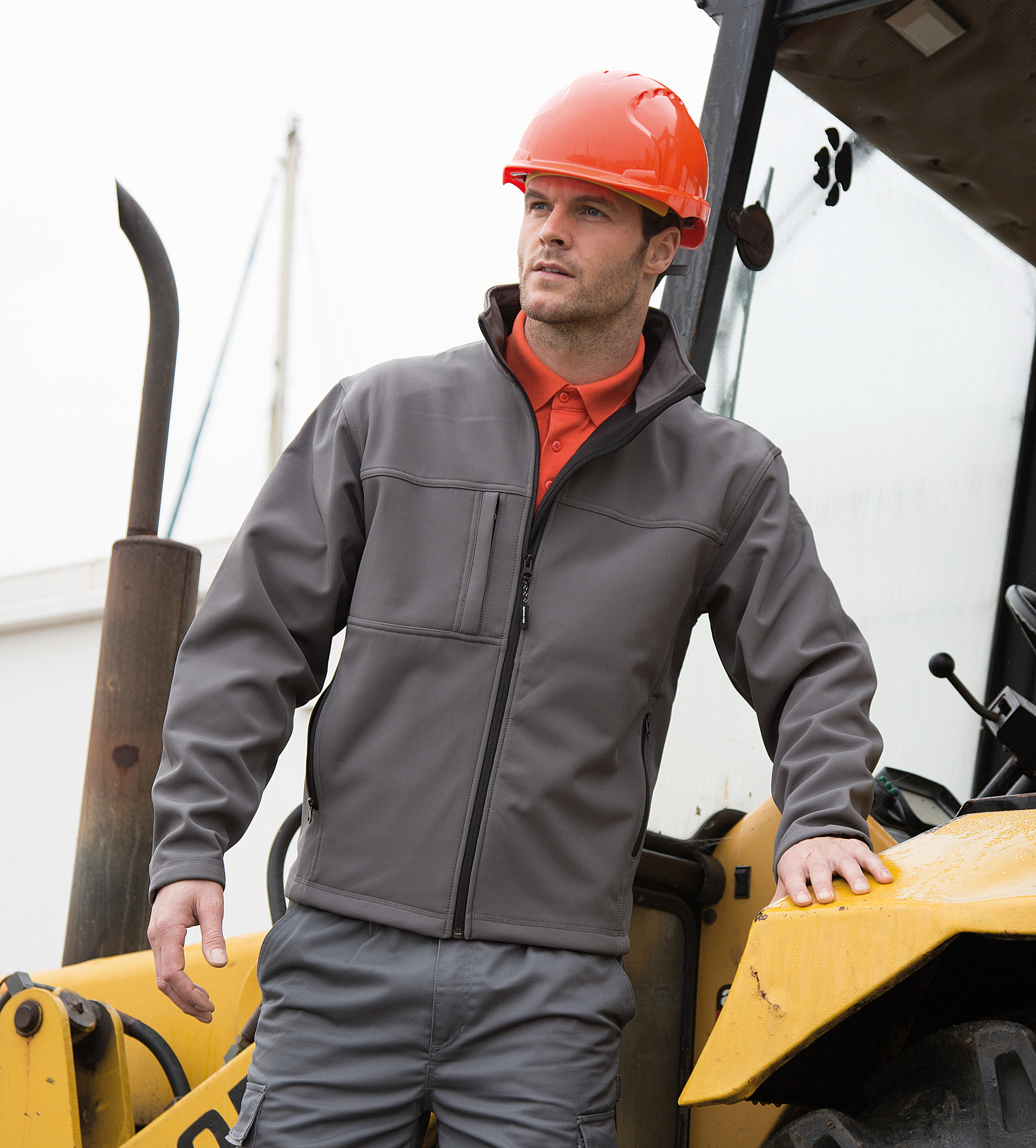 Trabajador con casco de obra naranja apoyado en una excavadora amarilla.