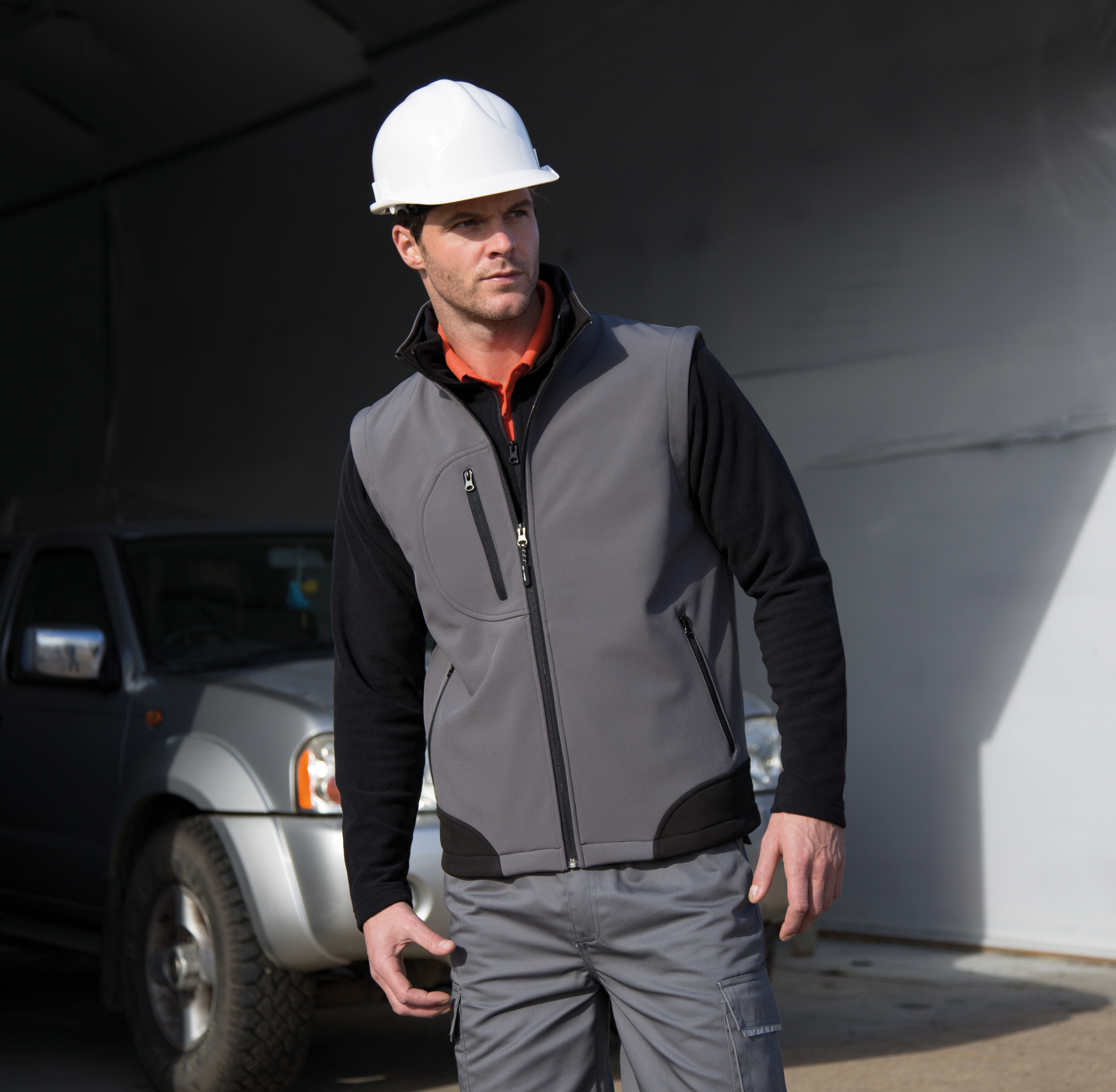 trabajador con casco blanco y chaleco gris junto a un vehículo industrial