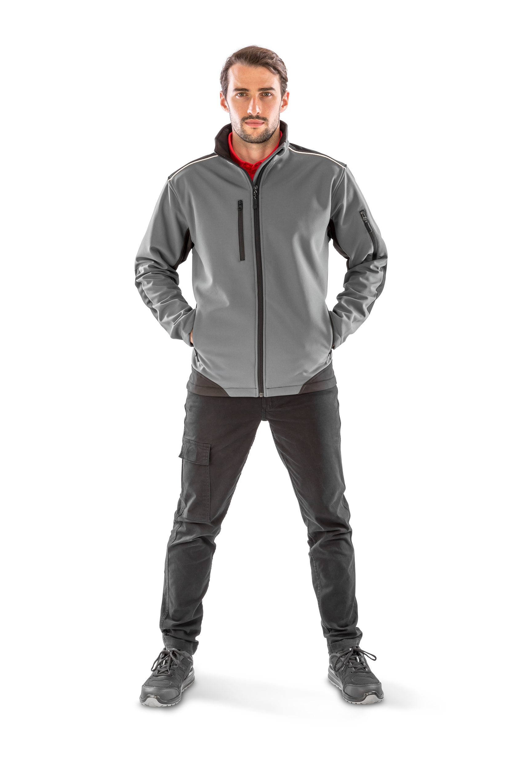 Hombre de pie con chaqueta gris de softshell y pantalones cargo negros sobre fondo blanco.