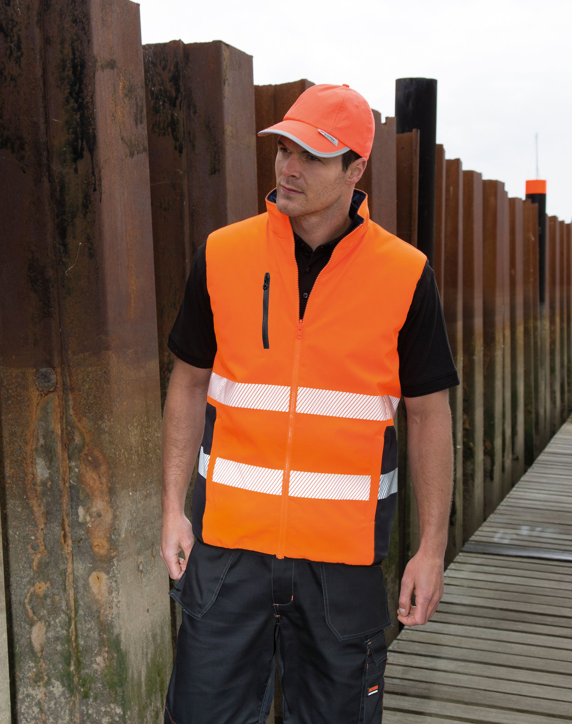 Trabajador junto a un muelle vistiendo chaleco y gorra de seguridad naranjas con bandas reflectantes