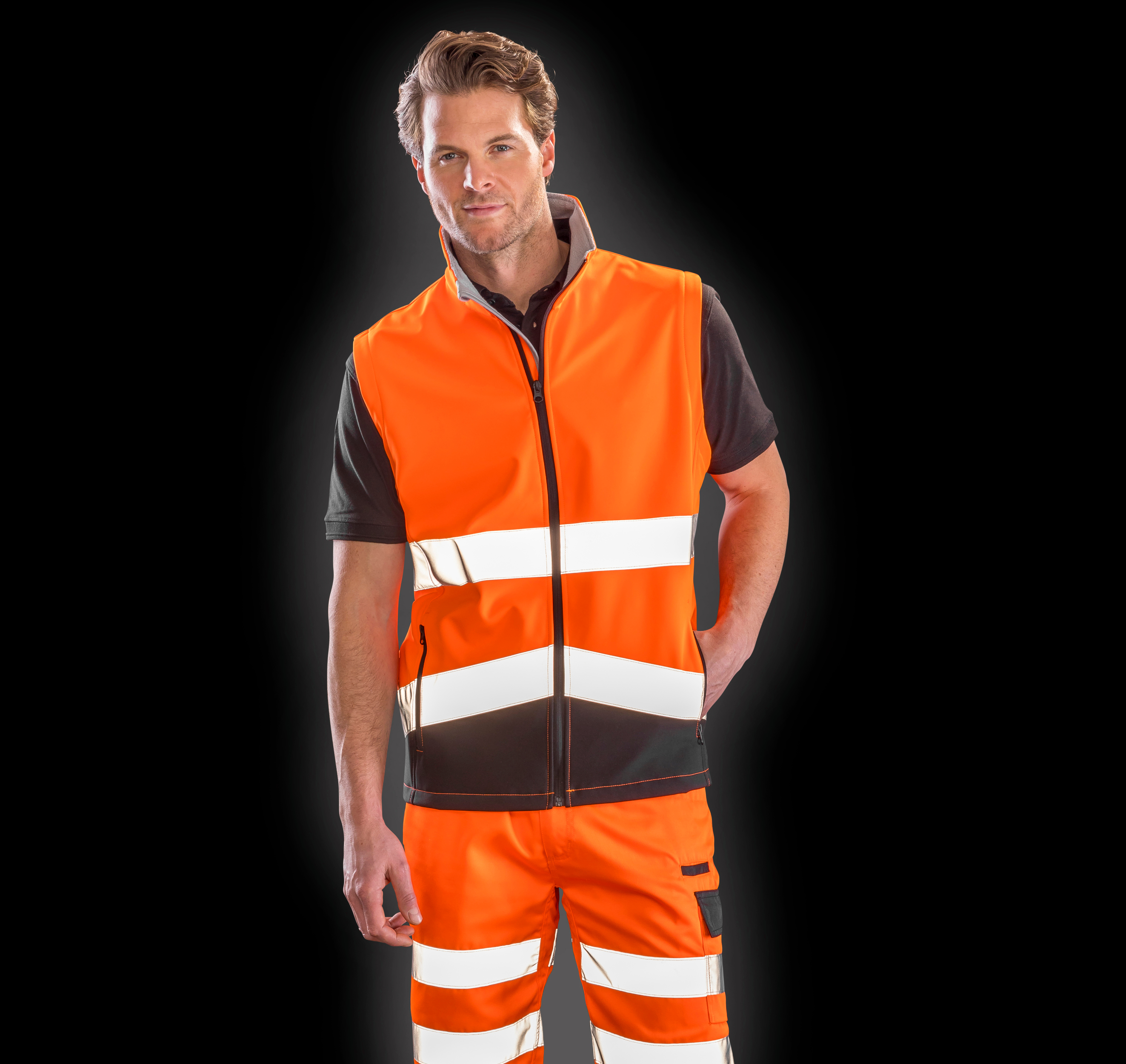 Hombre con chaleco y pantalones de alta visibilidad naranja con bandas reflectantes sobre fondo negro