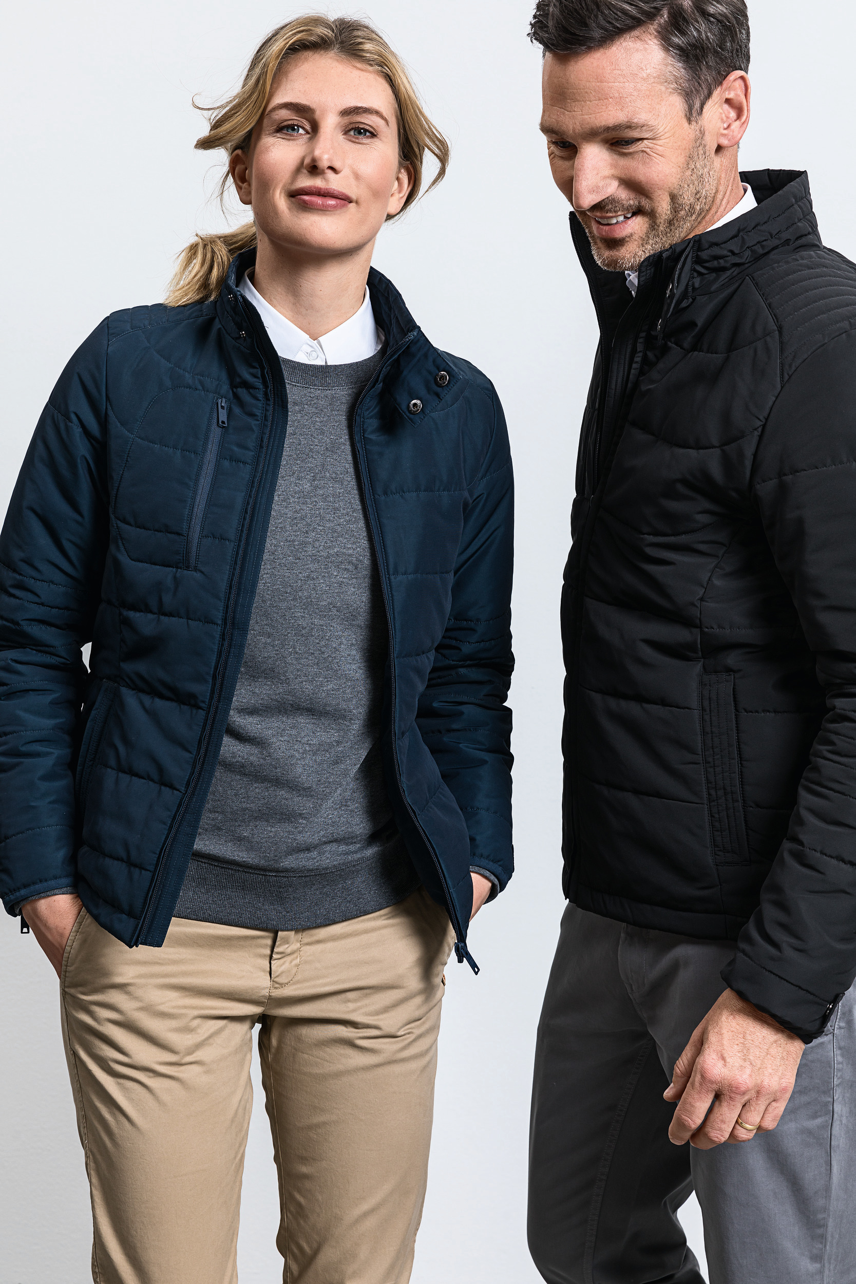 Pareja con chaquetas acolchadas y pantalones chinos sobre fondo blanco