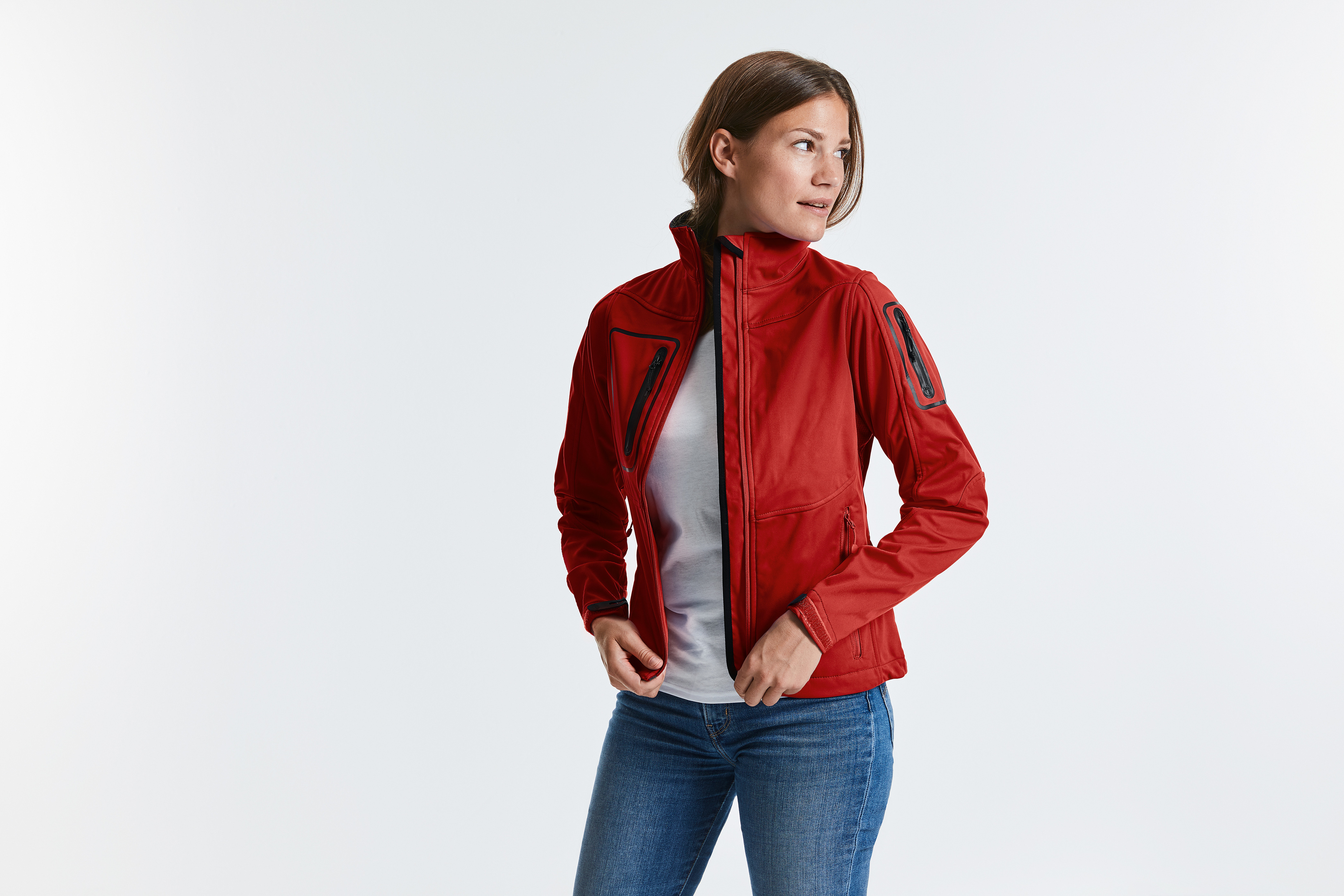 Mujer ajustándose una chaqueta softshell roja sobre fondo blanco