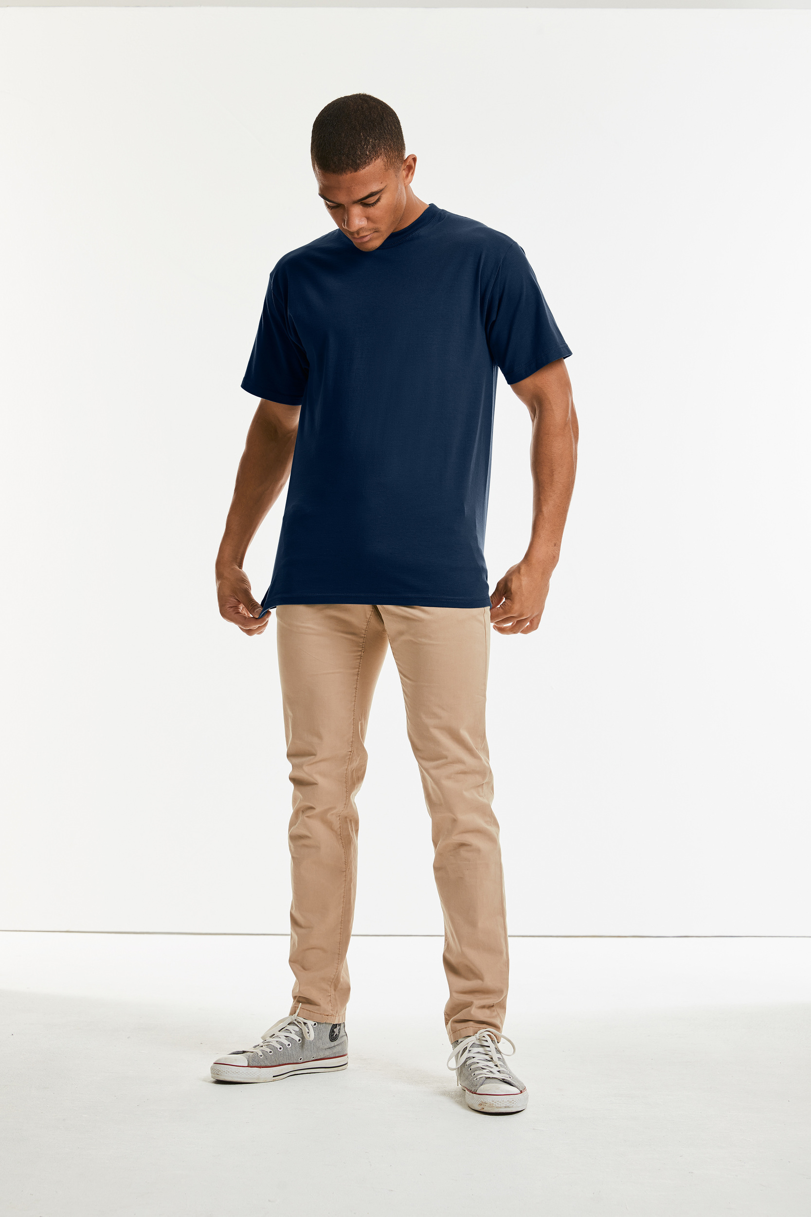 Modelo masculino con camiseta azul marino y pantalones chinos beige sobre fondo blanco.