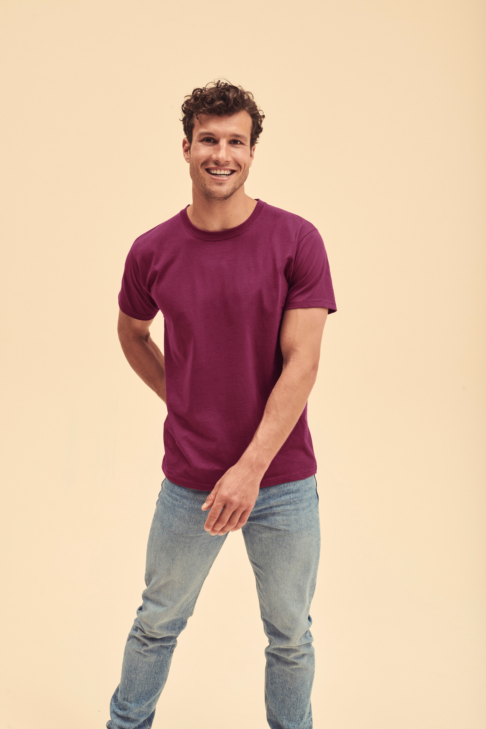 hombre sonriente de pie con camiseta morada y vaqueros sobre fondo claro