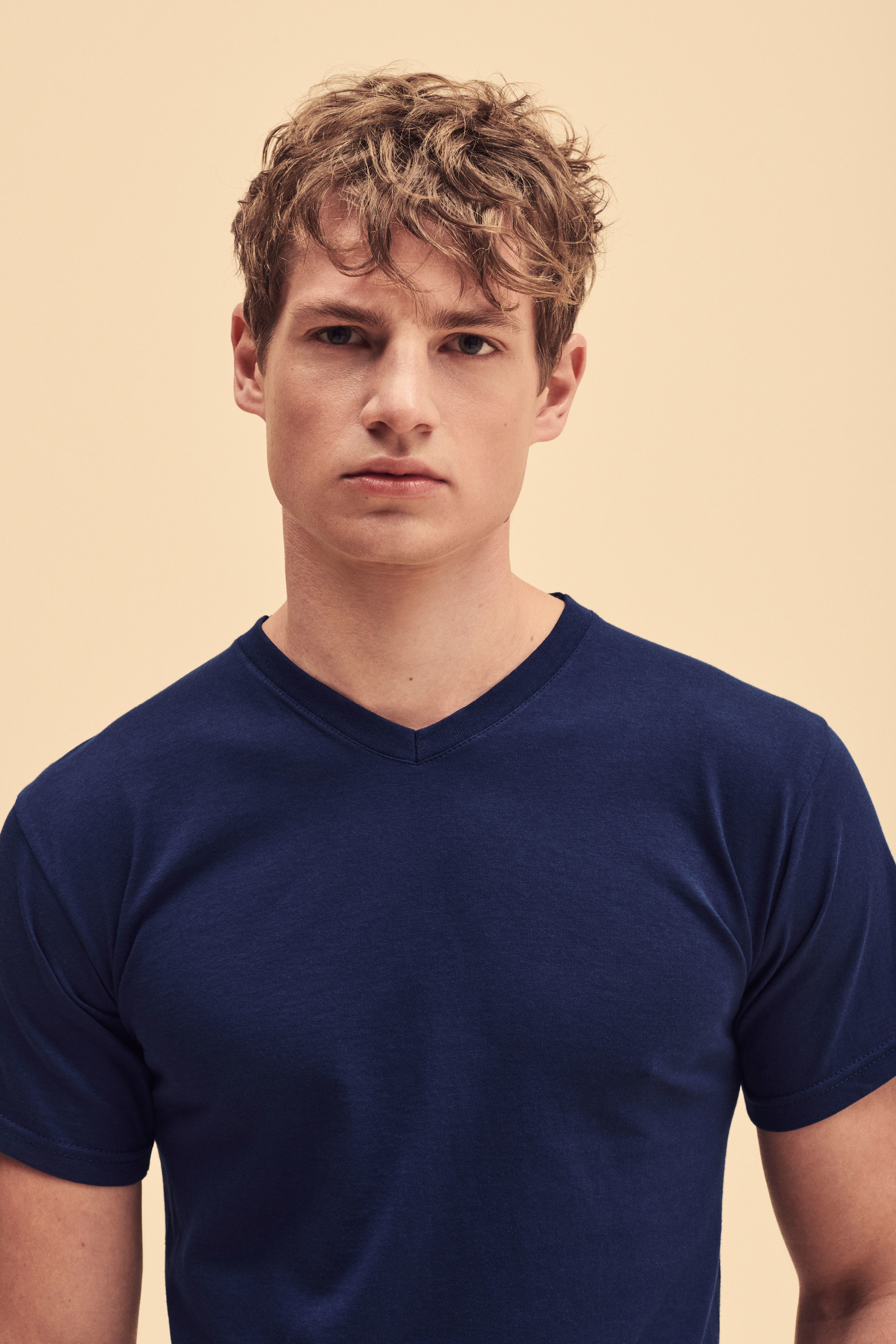 joven con camiseta azul de cuello de pico mirando al frente sobre fondo neutro beige