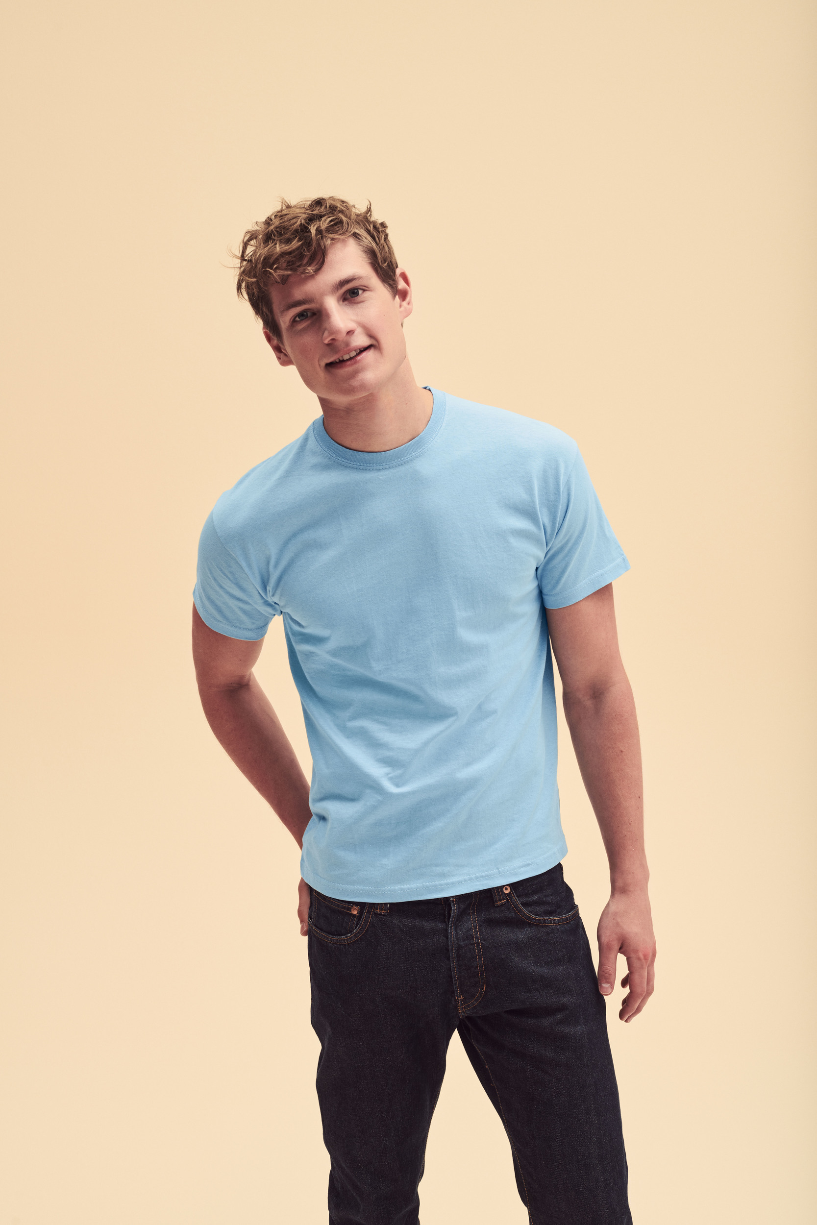 Joven con camiseta azul claro y vaqueros negros en fondo neutro claro