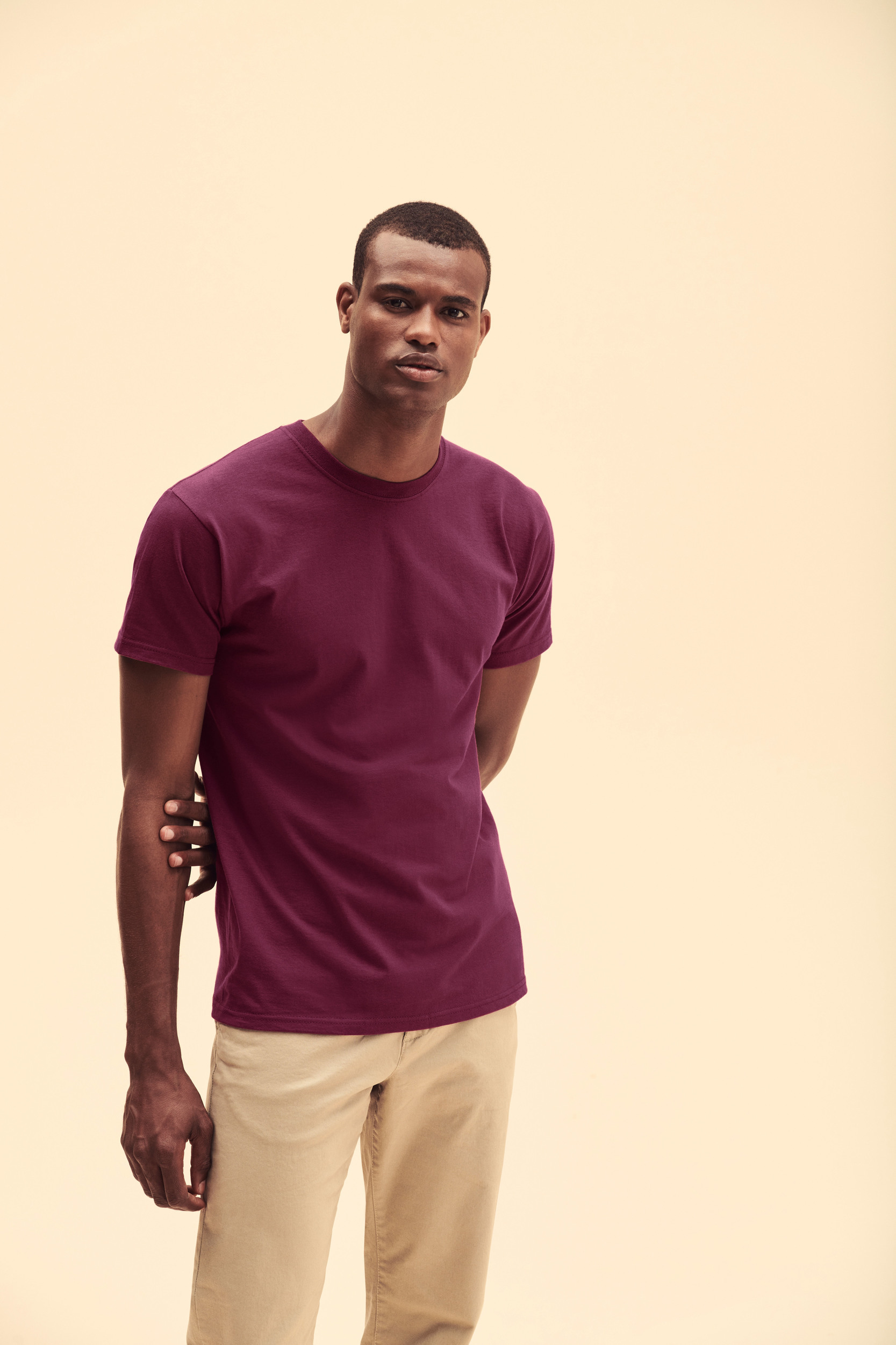 Hombre joven con camiseta morada y pantalones beige sobre fondo claro.