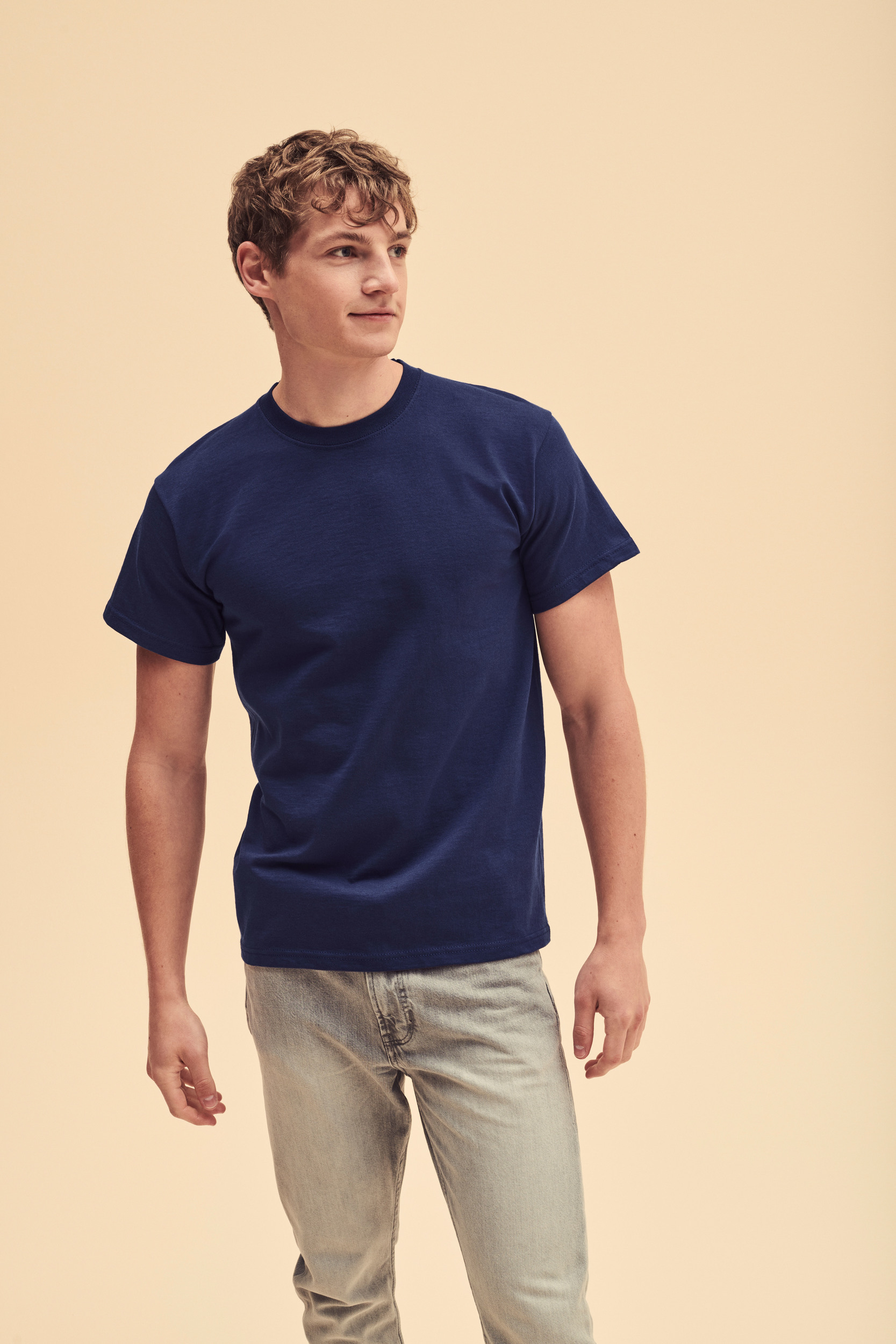 hombre joven de pie con camiseta azul marino y vaqueros claros sobre fondo beige