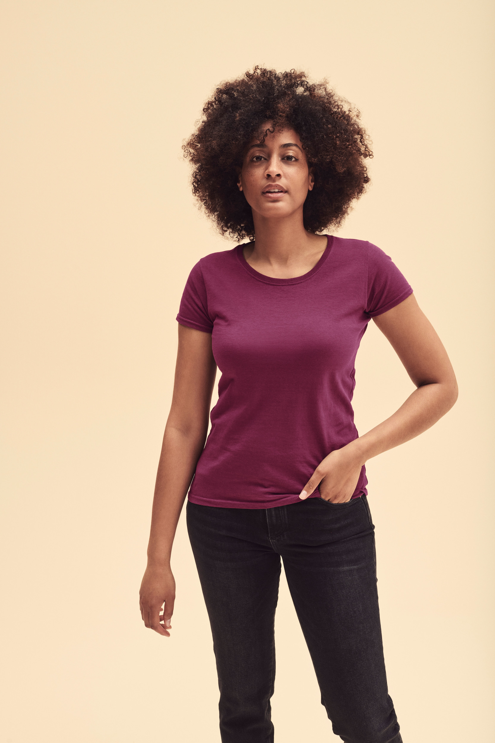 Mujer de pie con camiseta morada y vaqueros negros sobre fondo neutro