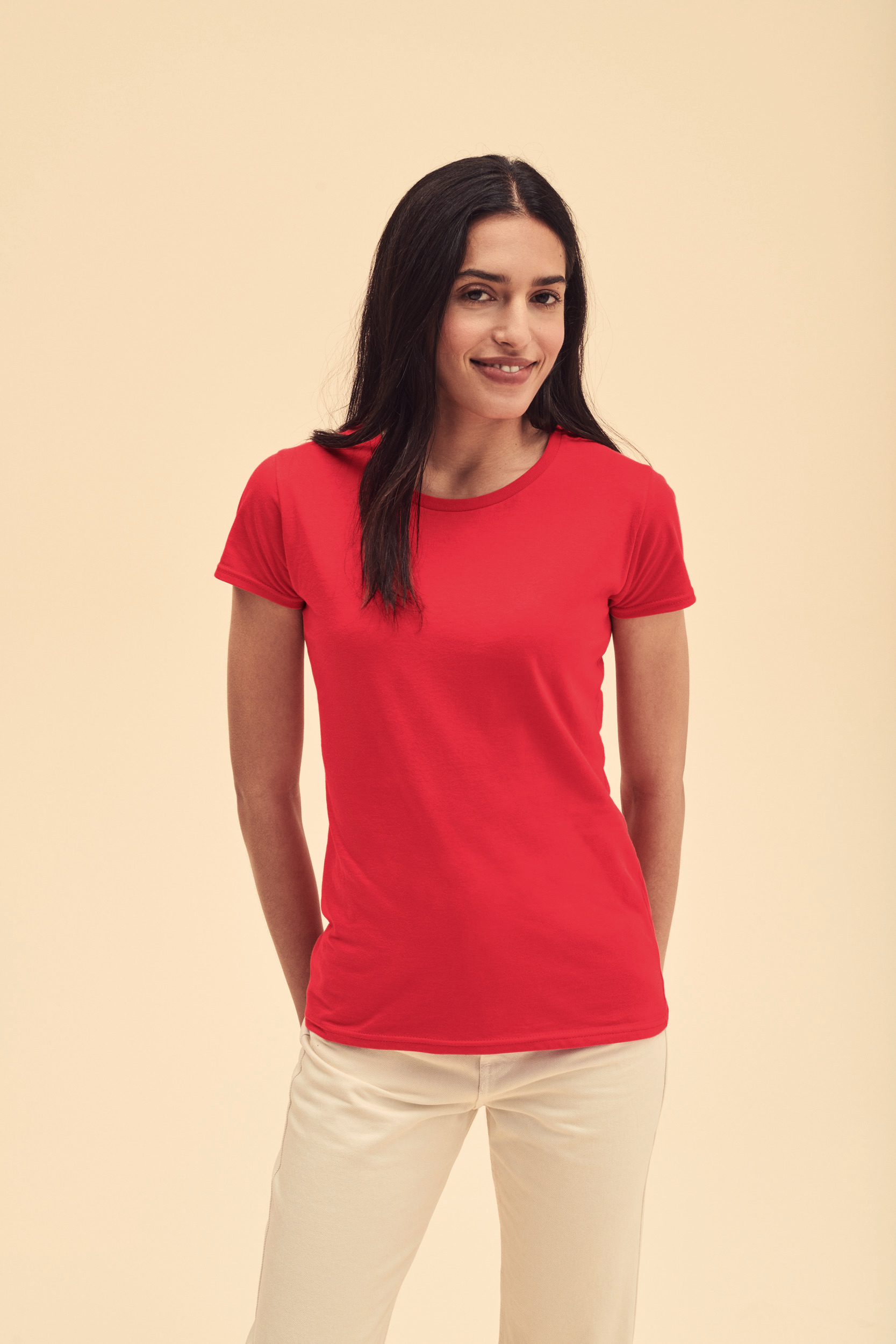 Mujer sonriente con camiseta roja de manga corta y pantalones claros sobre fondo neutro