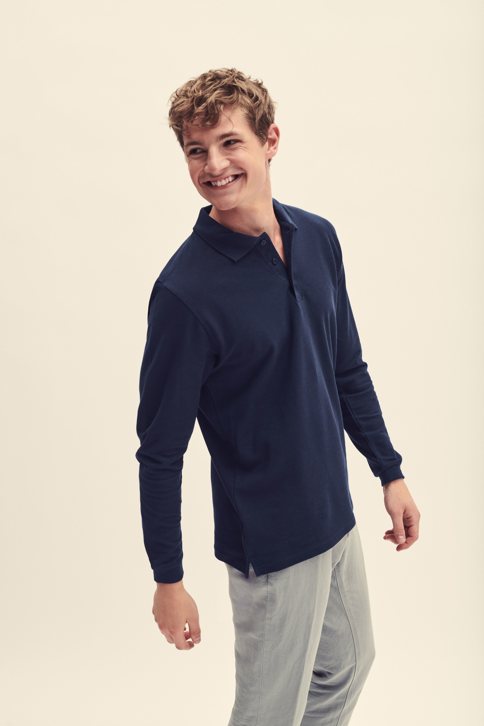 Hombre sonriente con polo azul marino de manga larga y pantalones grises sobre fondo claro