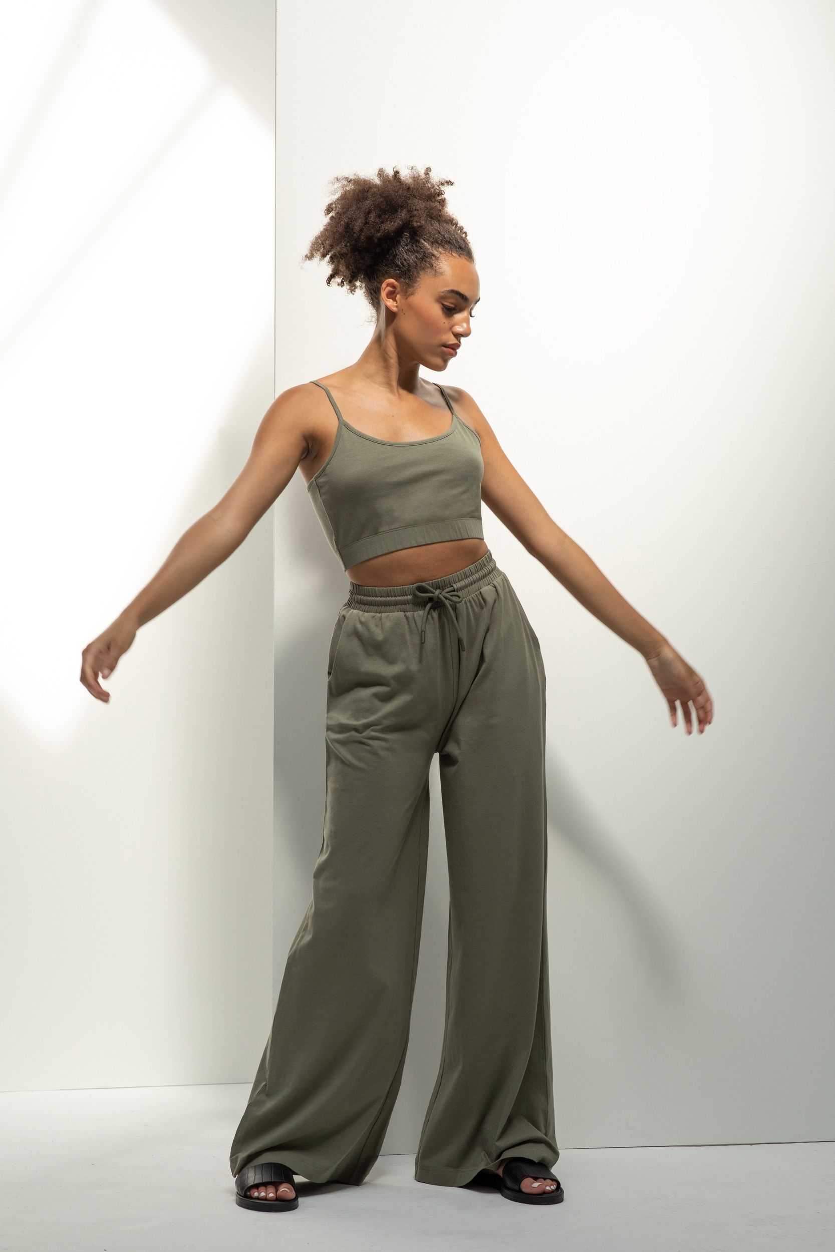 Mujer joven con conjunto verde caqui de top corto y pantalón ancho posando sobre fondo blanco