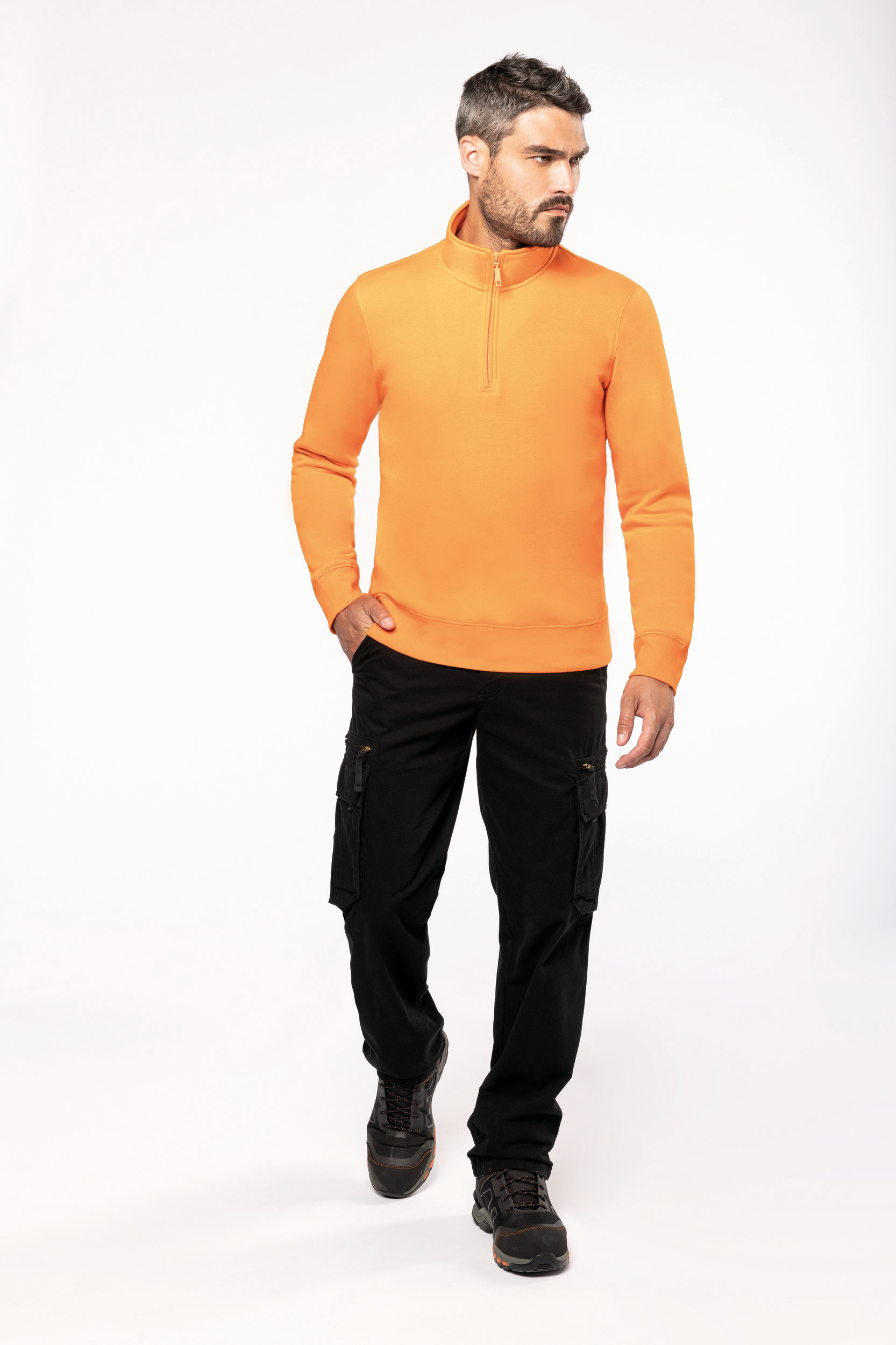 Hombre con forro polar naranja de media cremallera y pantalones cargo negros caminando sobre fondo blanco