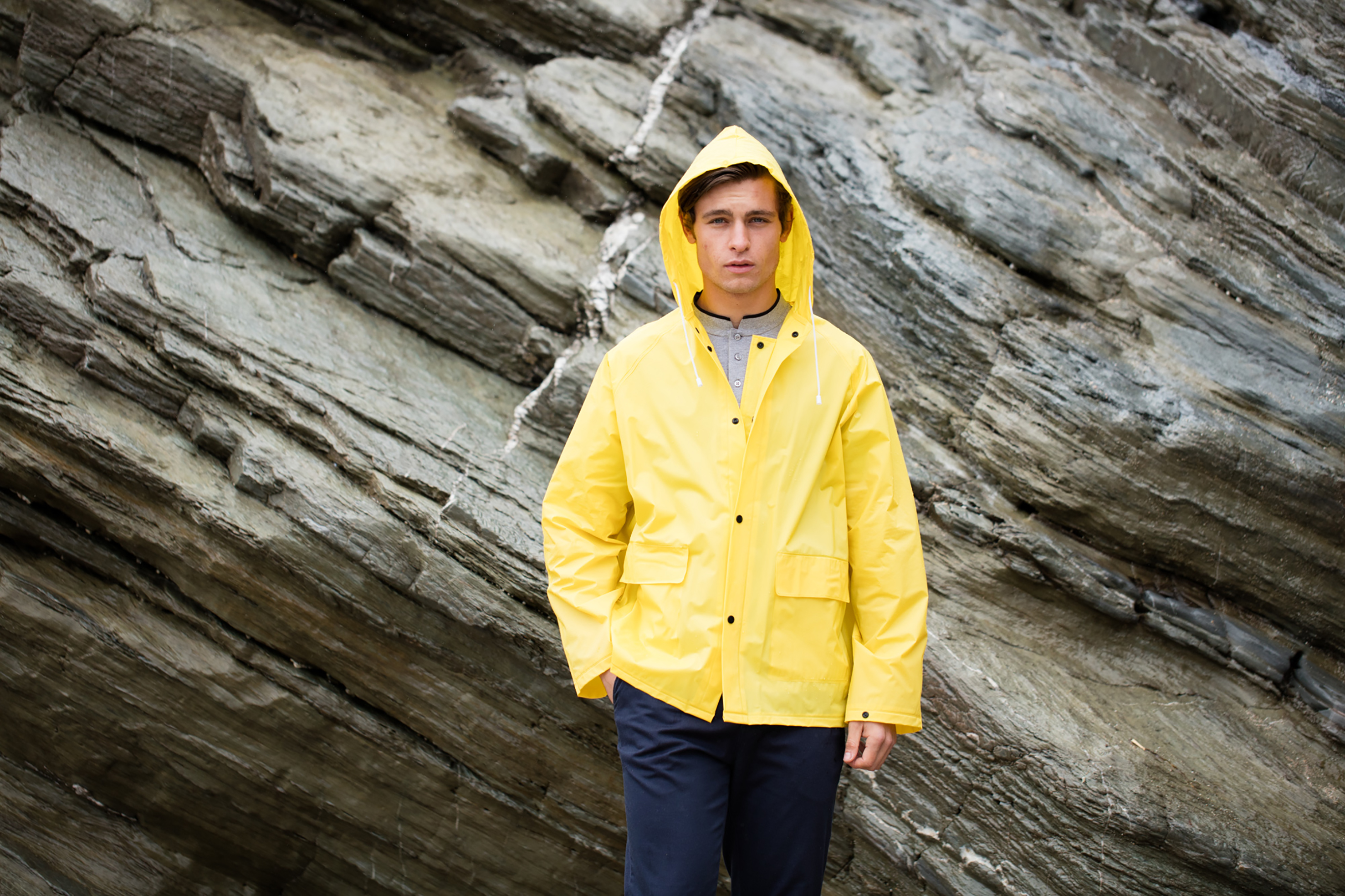 Hombre con chubasquero amarillo con capucha frente a una pared rocosa