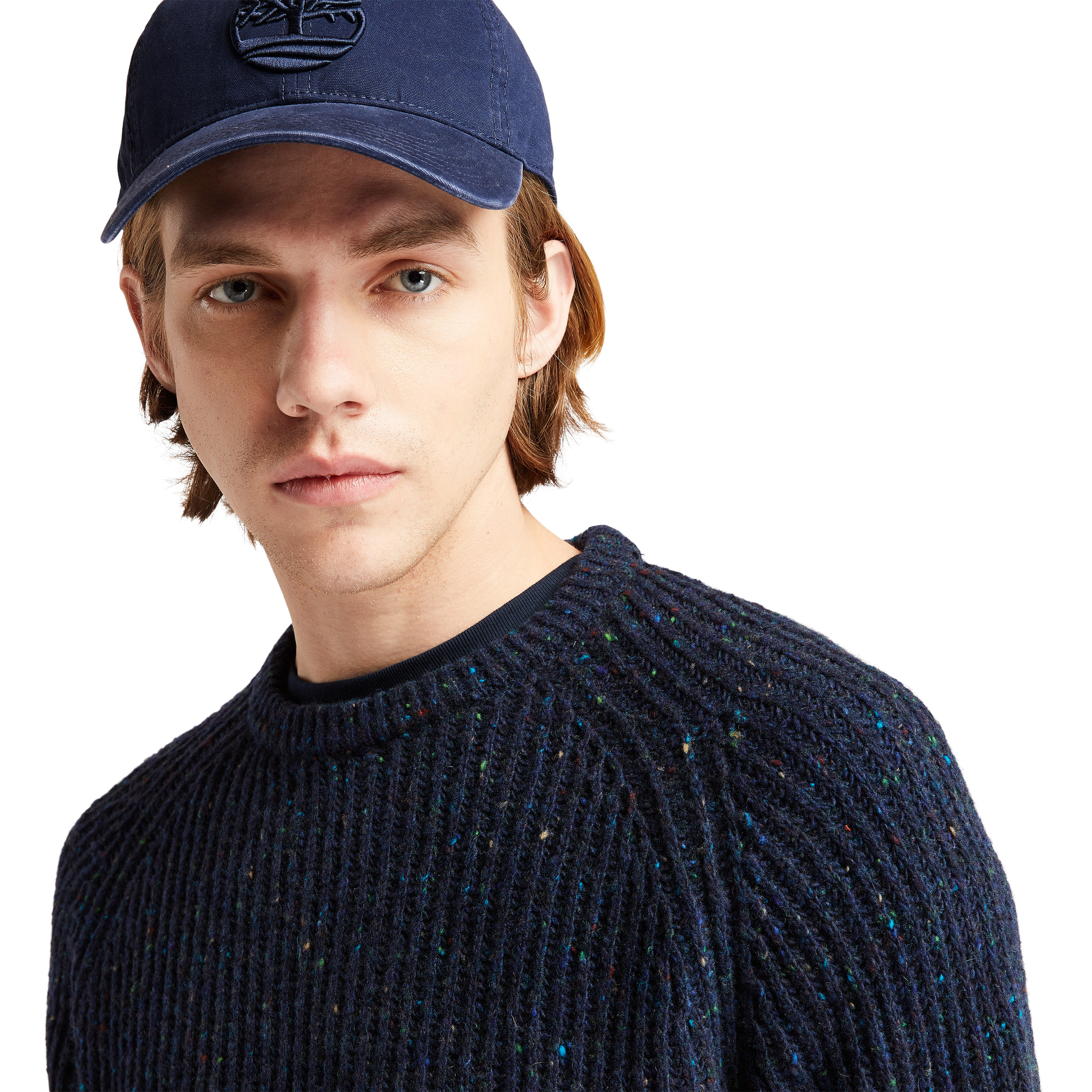 hombre joven con gorra azul y jersey de punto oscuro sobre fondo blanco