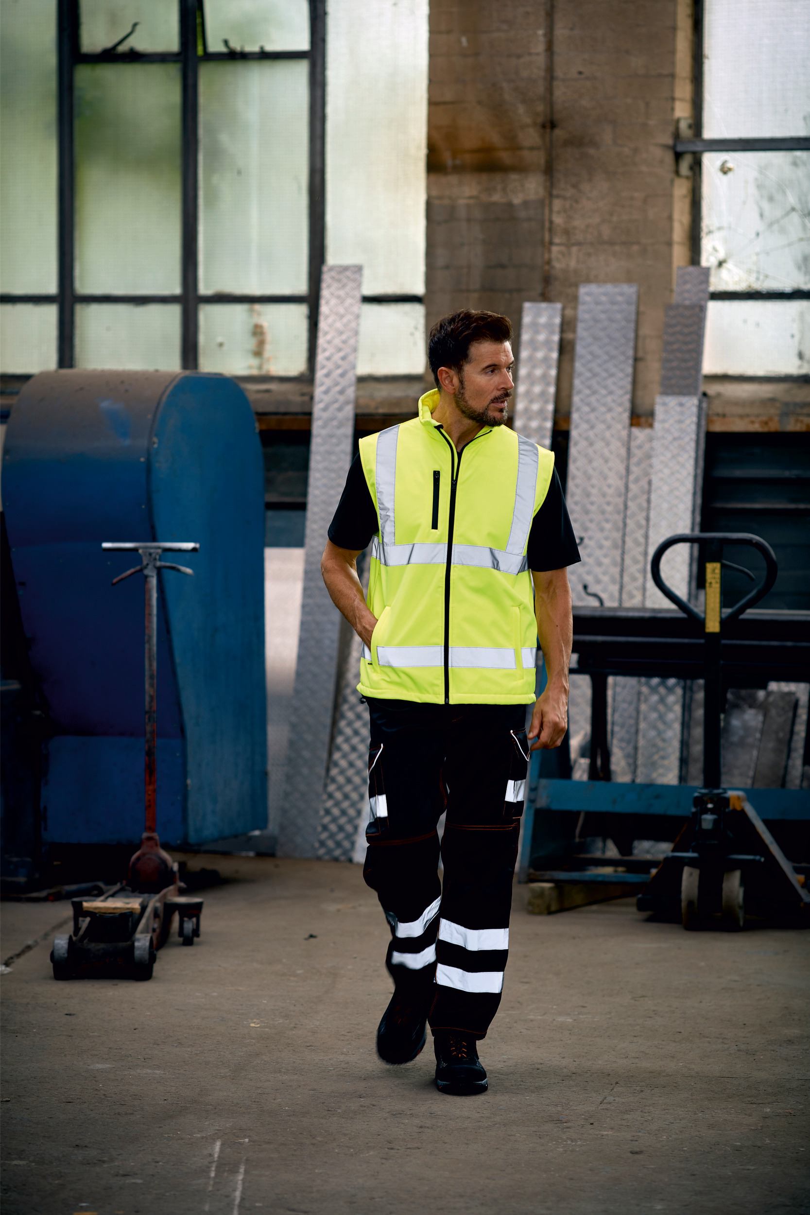 hombre con chaleco de alta visibilidad y pantalones reflectantes caminando en un taller industrial