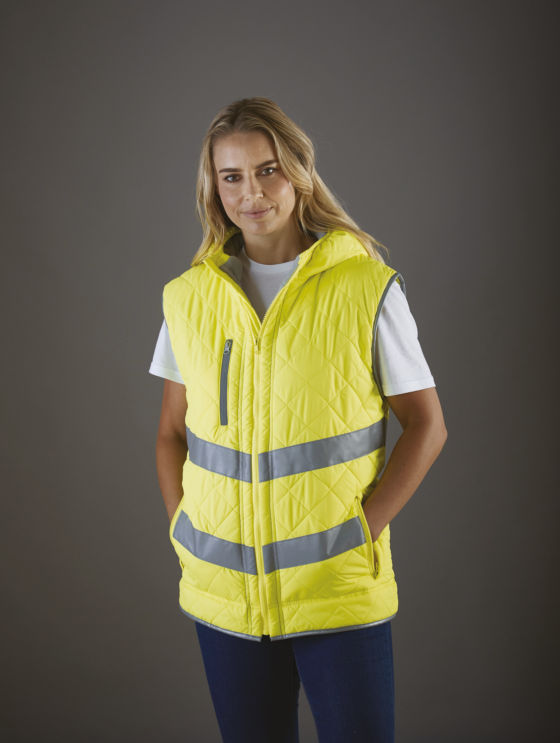 mujer con chaleco acolchado amarillo reflectante sobre camiseta blanca y fondo neutro