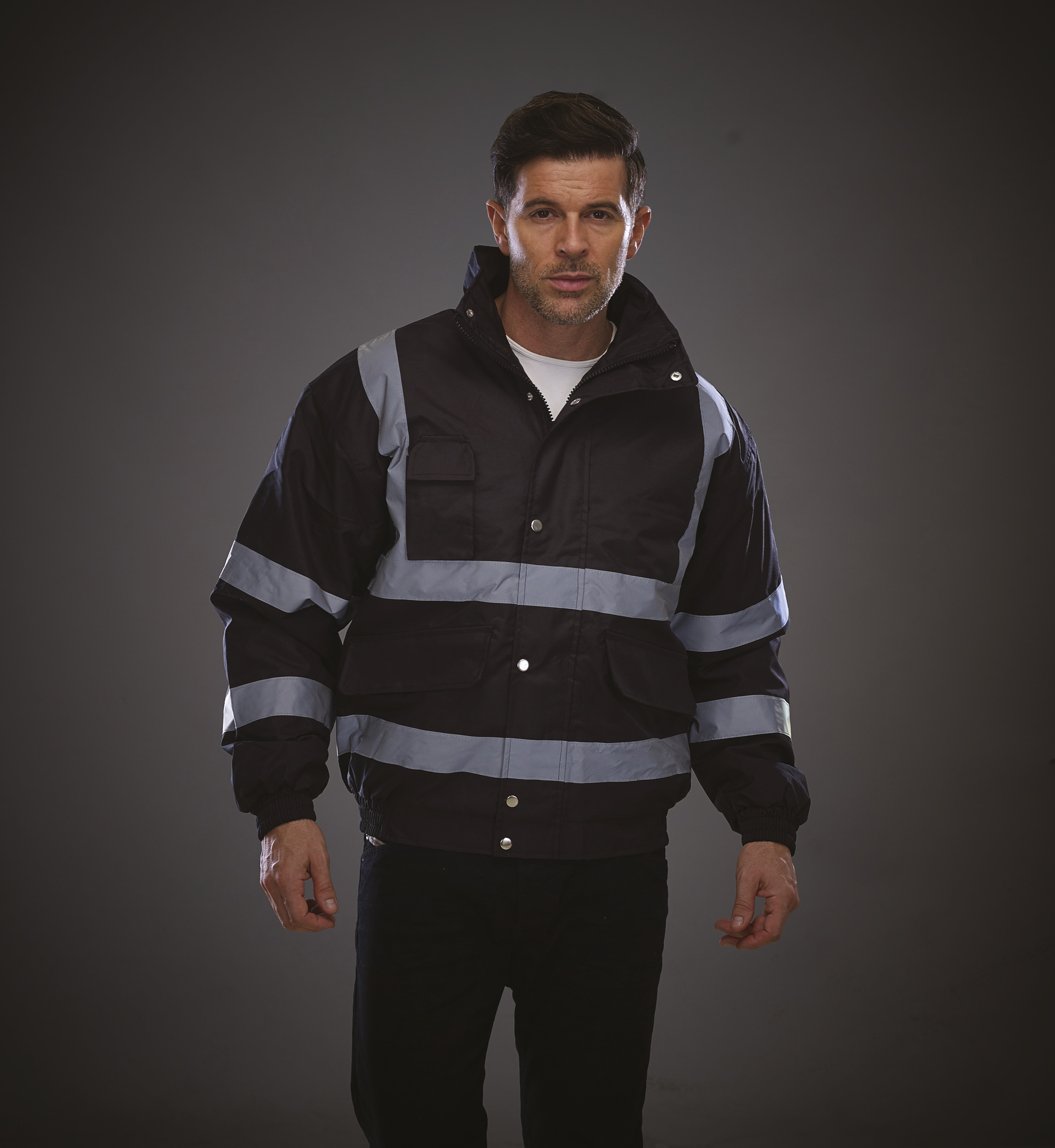 Hombre con chaqueta de alta visibilidad negra y bandas reflectantes sobre fondo gris oscuro