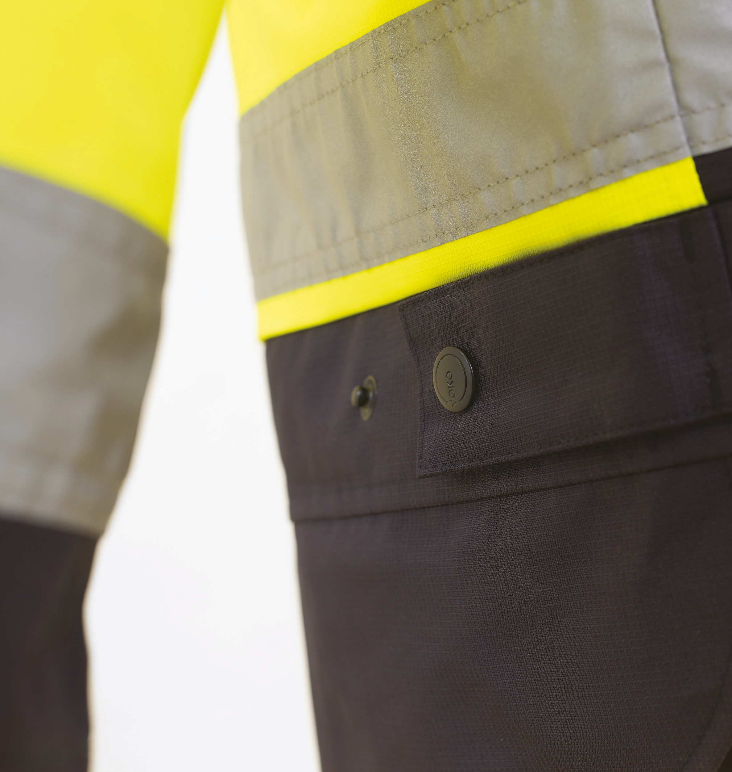 Detalle de chaqueta de alta visibilidad amarilla con franja reflectante y pantalón de trabajo negro con bolsillo abotonado.