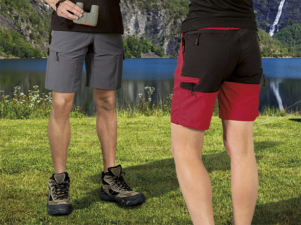 Dos personas de pie con pantalones cortos de senderismo y botas junto a un lago de montaña.