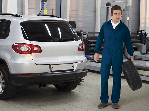 técnico de taller sujetando una rueda junto a un SUV blanco en el taller automóvilístico