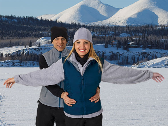 Pareja joven abrazada con ropa de invierno sobre un lago helado y montañas nevadas al fondo