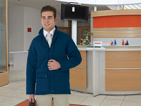 Hombre joven con chaqueta azul y maletín junto a la recepción de un hotel moderno