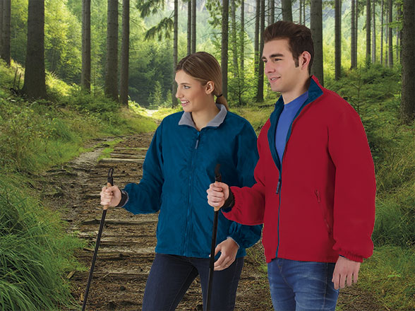 Pareja joven con chaquetas y bastones de senderismo caminando por un sendero en el bosque