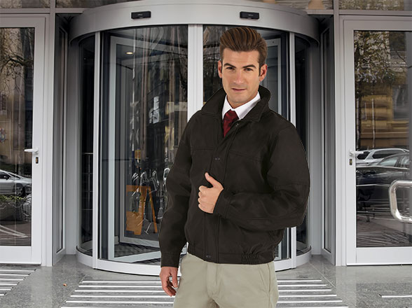 hombre con chaqueta oscura de estilo bomber frente a la puerta giratoria de un edificio moderno