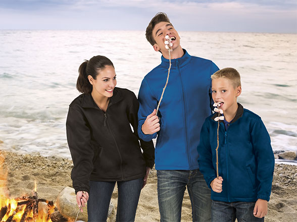 Mujer, hombre y niño tuestan malvaviscos junto a una hoguera en la orilla de la playa