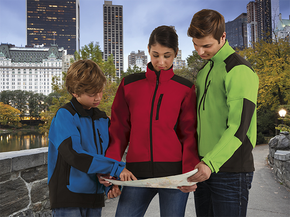 Tres personas (un niño, una mujer y un hombre) con chaquetas de colores revisando un mapa en un parque urbano con rascacielos de fondo