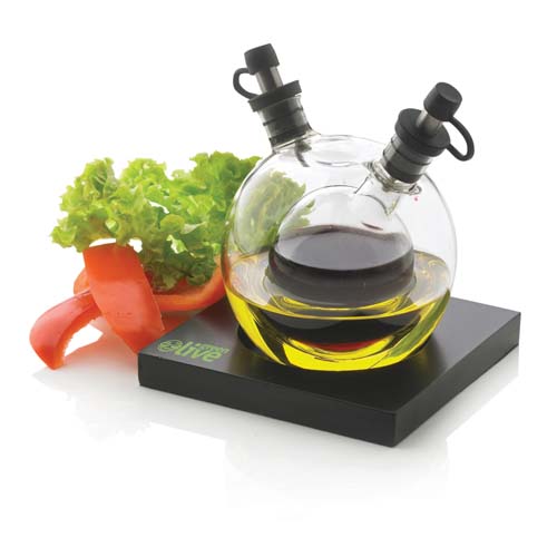 Aceitera y vinagrera de cristal redondas sobre base negra junto a lechuga y tiras de pimiento rojo.